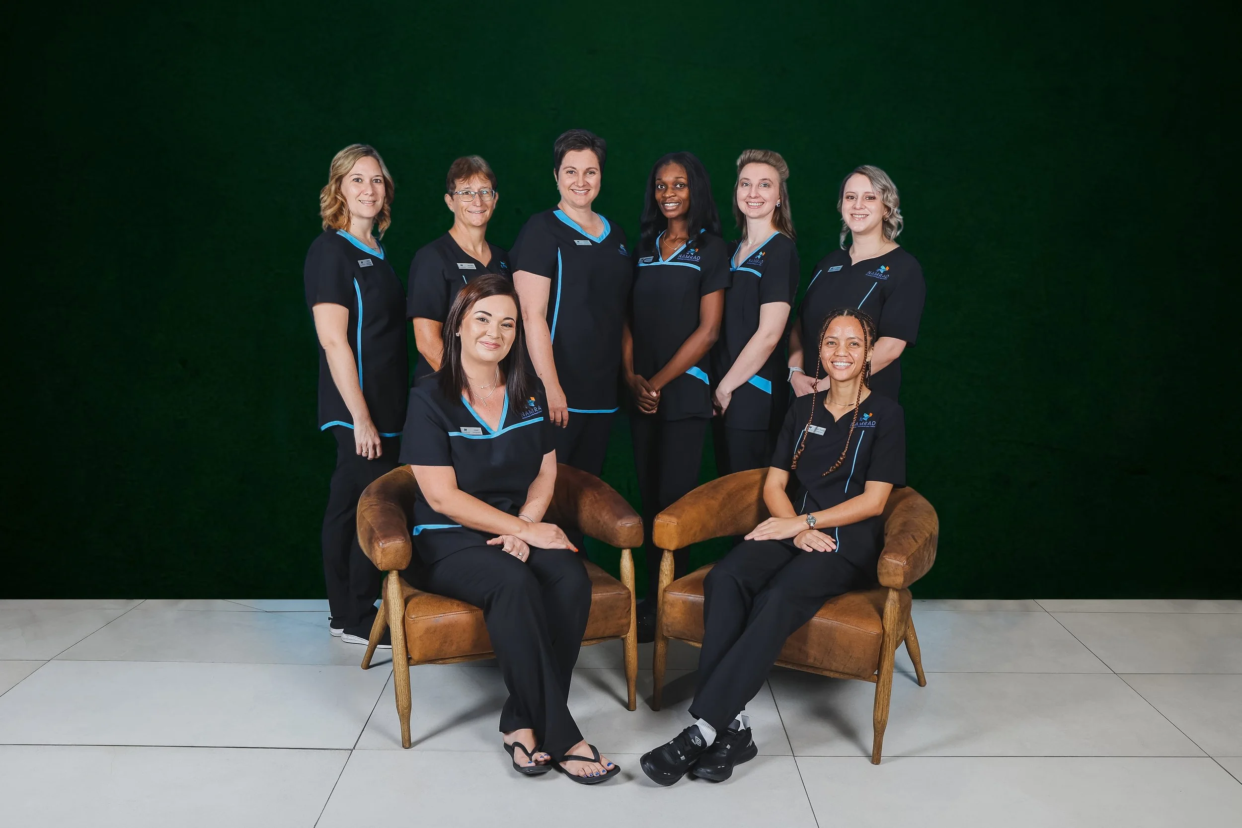 Eight ladies in black scrubs in front of a green wall