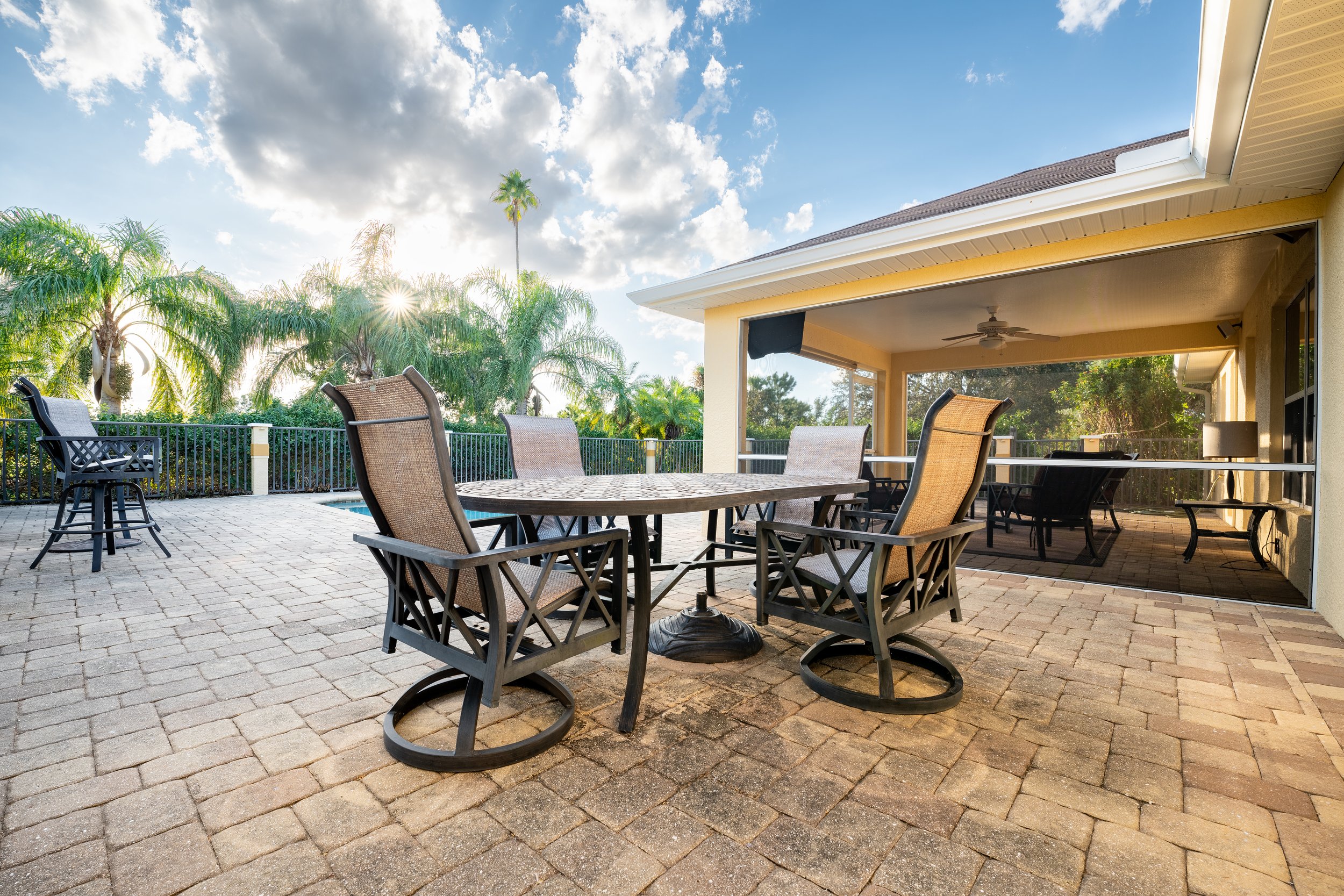 Outdoor patio with table, chairs, and palm trees in sunny setting.