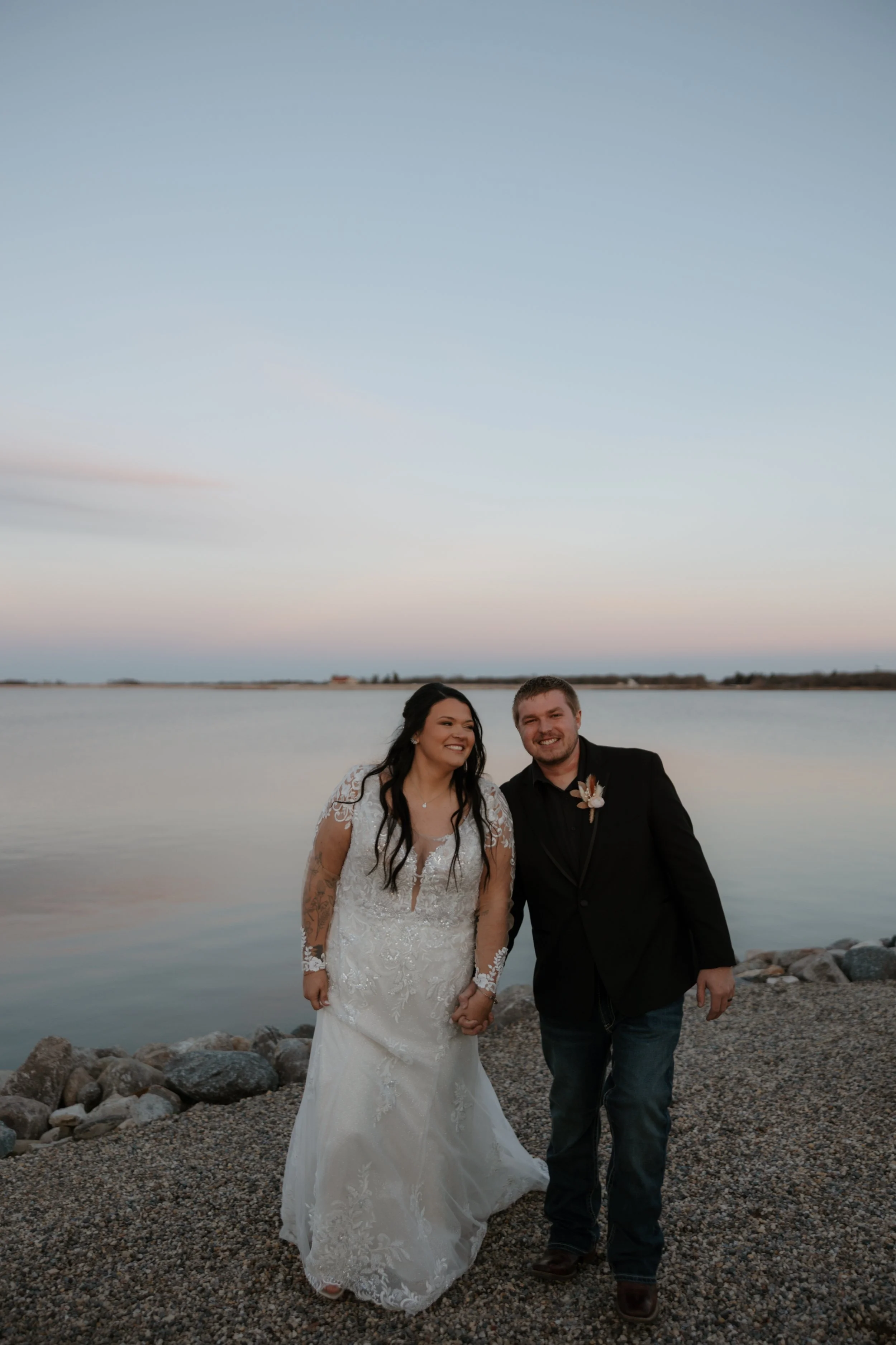 Elegant banquet hall decorated for an event with a table centerpiece featuring three candles, dried pampas grass, black napkins, and glassware, overlooking a waterfront view through large windows.