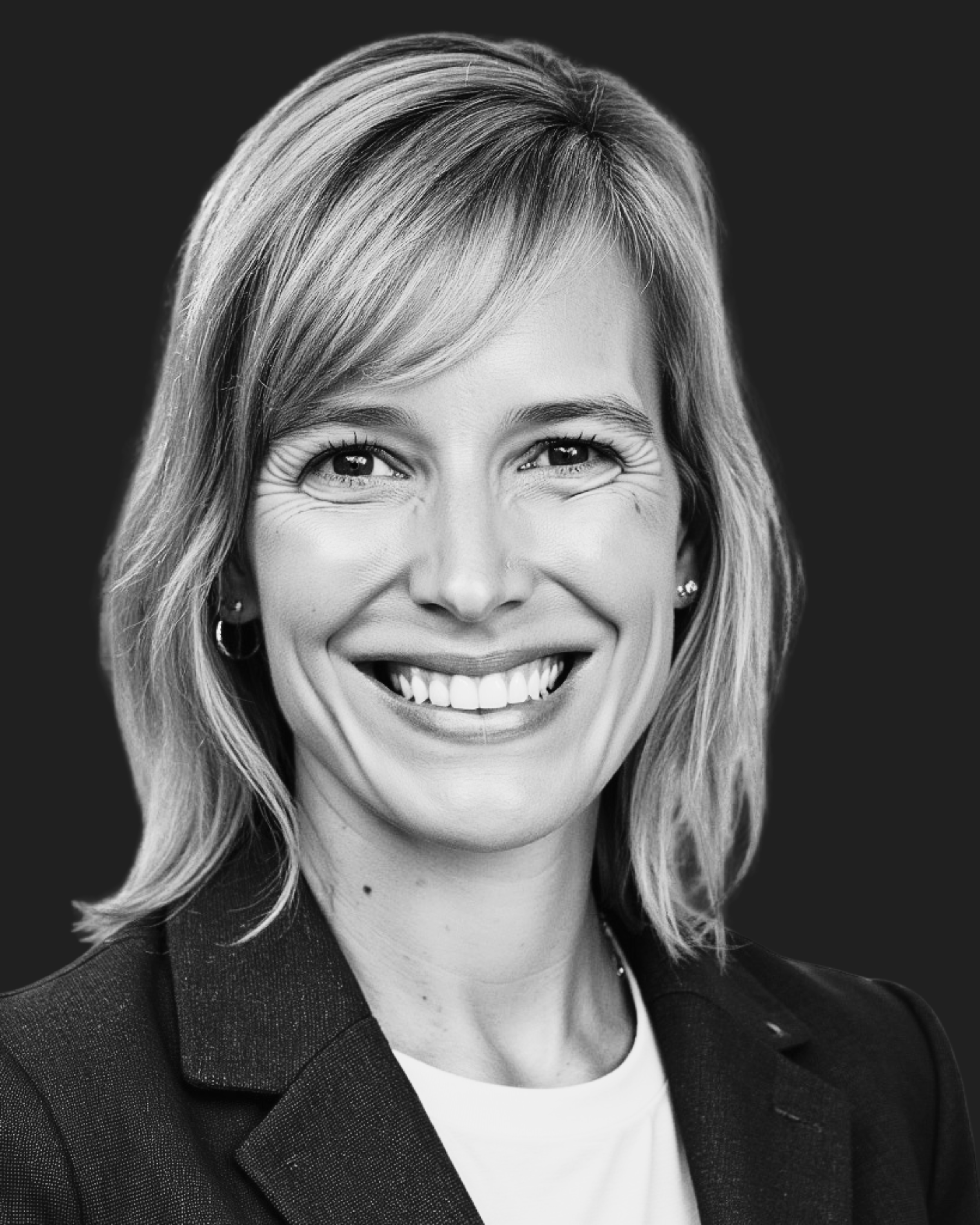 Black and white headshot of a woman with shoulder-length wavy hair, smiling, wearing a blazer and earrings.