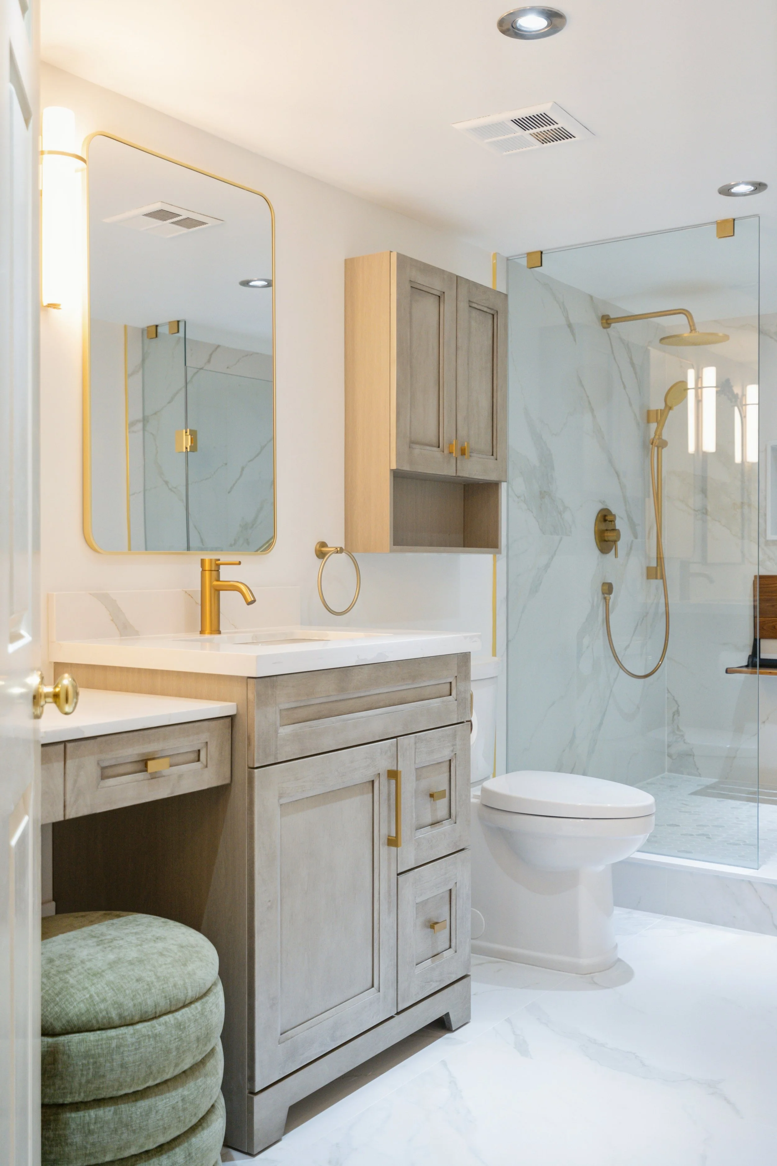 A modern bathroom with wood cabinets, gold fixtures, a mirror, a toilet, and a glass shower with marble walls and a gold showerhead.