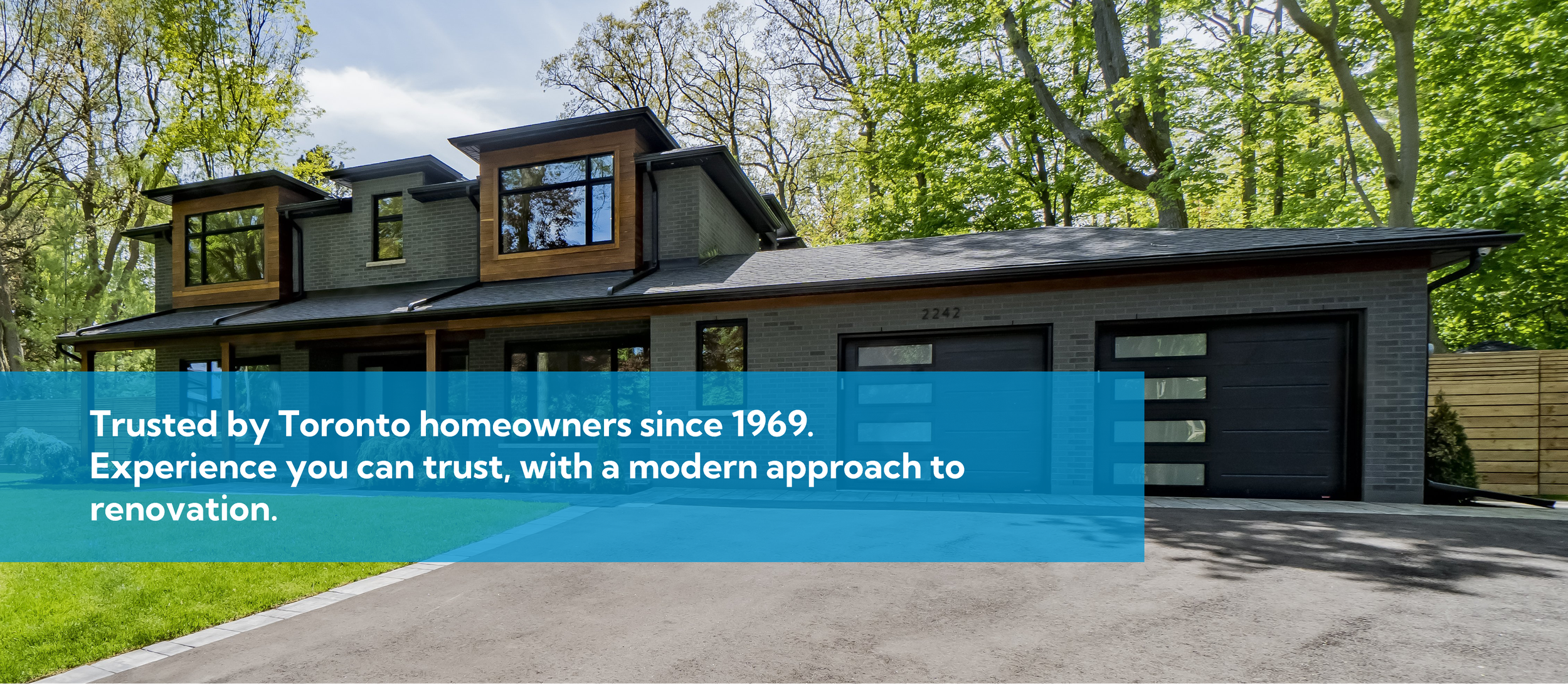 Modern two-story house with brick exterior, black garage doors, large windows, and wooden accents, surrounded by trees and a driveway.