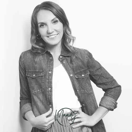 Black and white photo of a smiling woman with wavy hair, wearing a denim jacket and a white top, standing against a plain background.