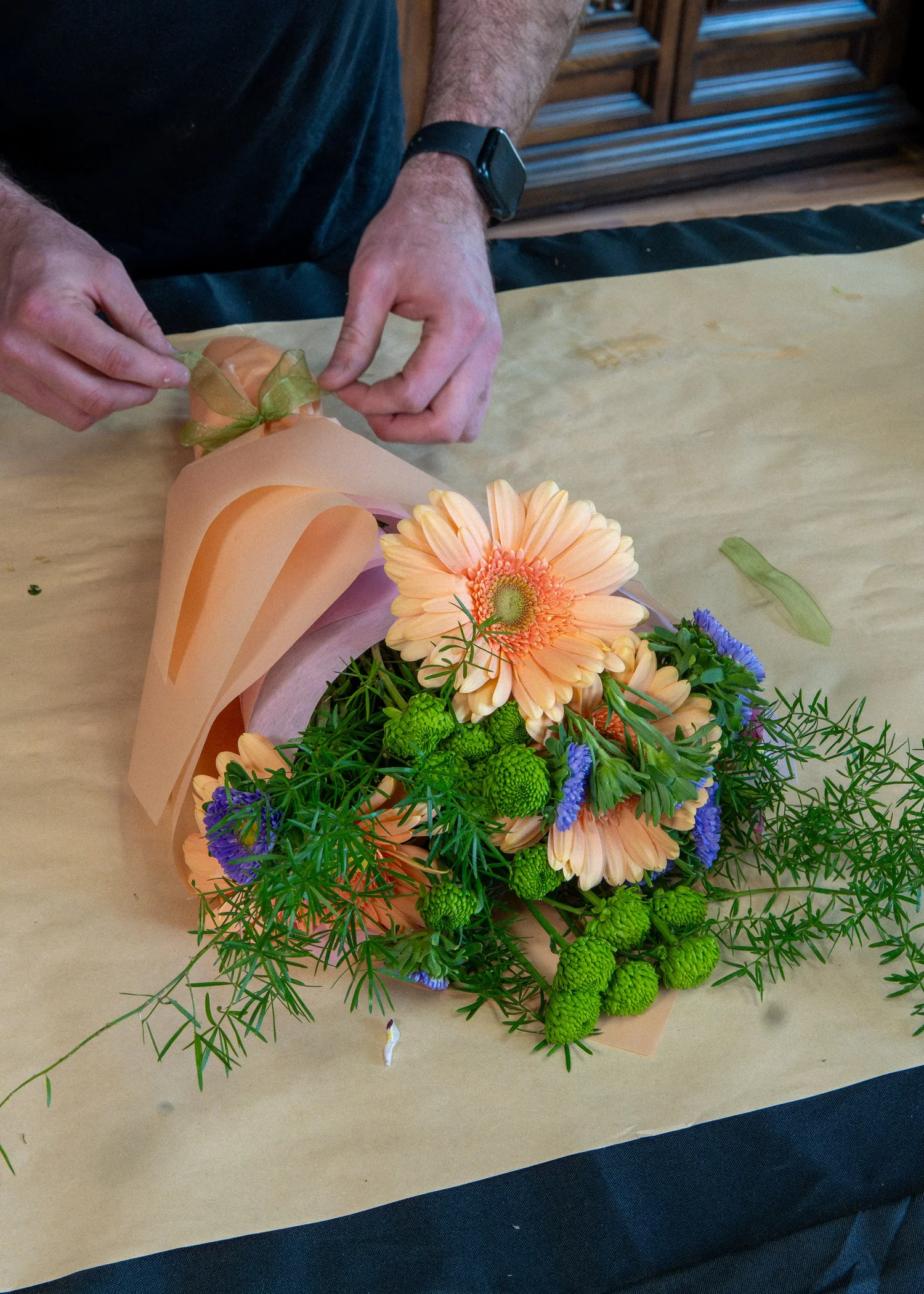 A hand-wrapped Esotarium bouquet with peach gerbera daisies, green flowers and blue accents.