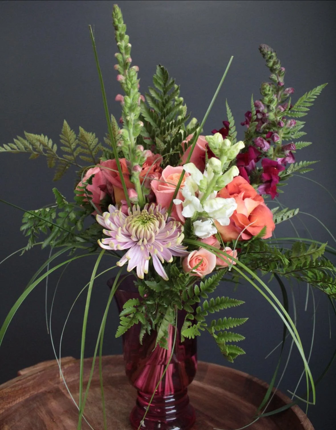 The Esotarium Bouquet with coral roses, pale lilac chrysanthemum, snapdragons and fern against a dark background.