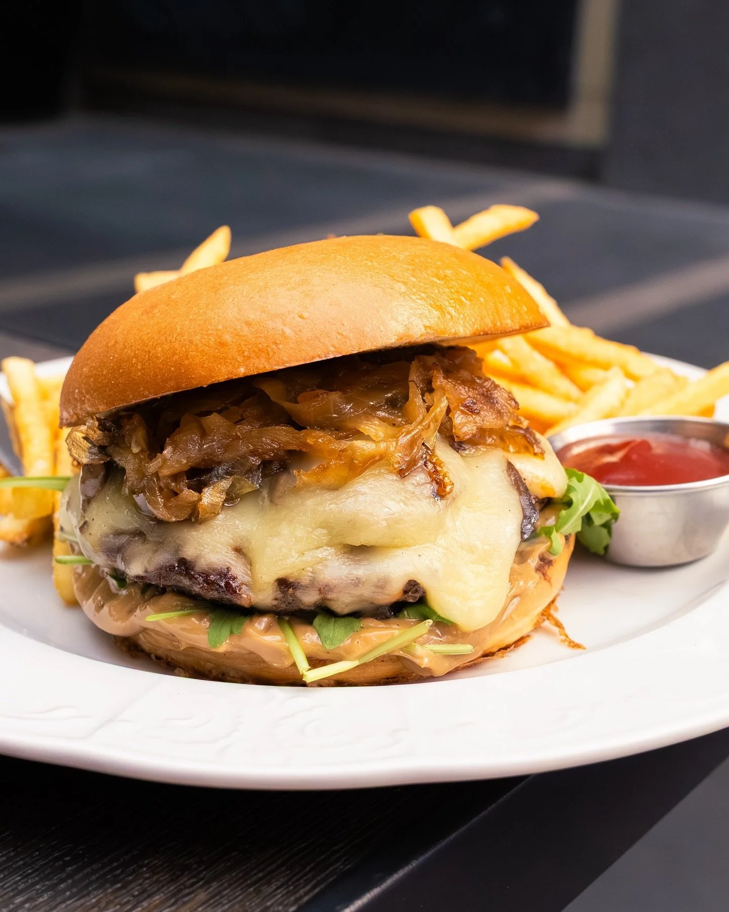 Flat-Top Burger, stacked with a juicy 6 oz. grilled beef patty, local mushrooms, caramelized onions, fontina, arugula, and black garlic aioli on a toasted brioche bun, served with golden crispy fries. Enjoy it here with us or take it to-go by. Takeaw