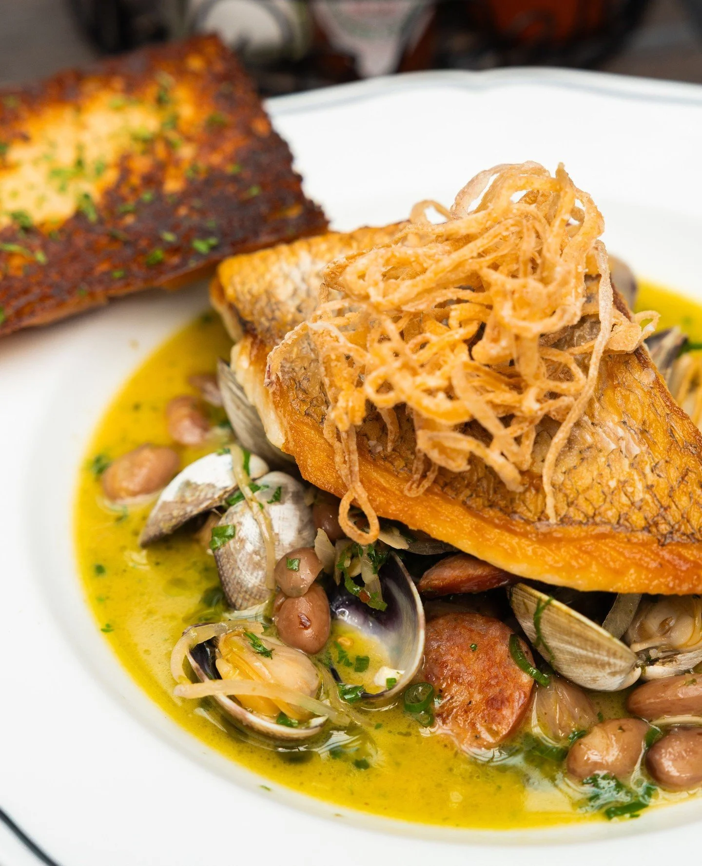 Our kind of summer supper. 🐟 Pan-roasted Red Snapper with clams and andouille, shelling beans, and a white wine-wild ramp butter sauce, finished with crispy shallots and served alongside griddled garlic bread. Pop by for dinner this weekend, and che