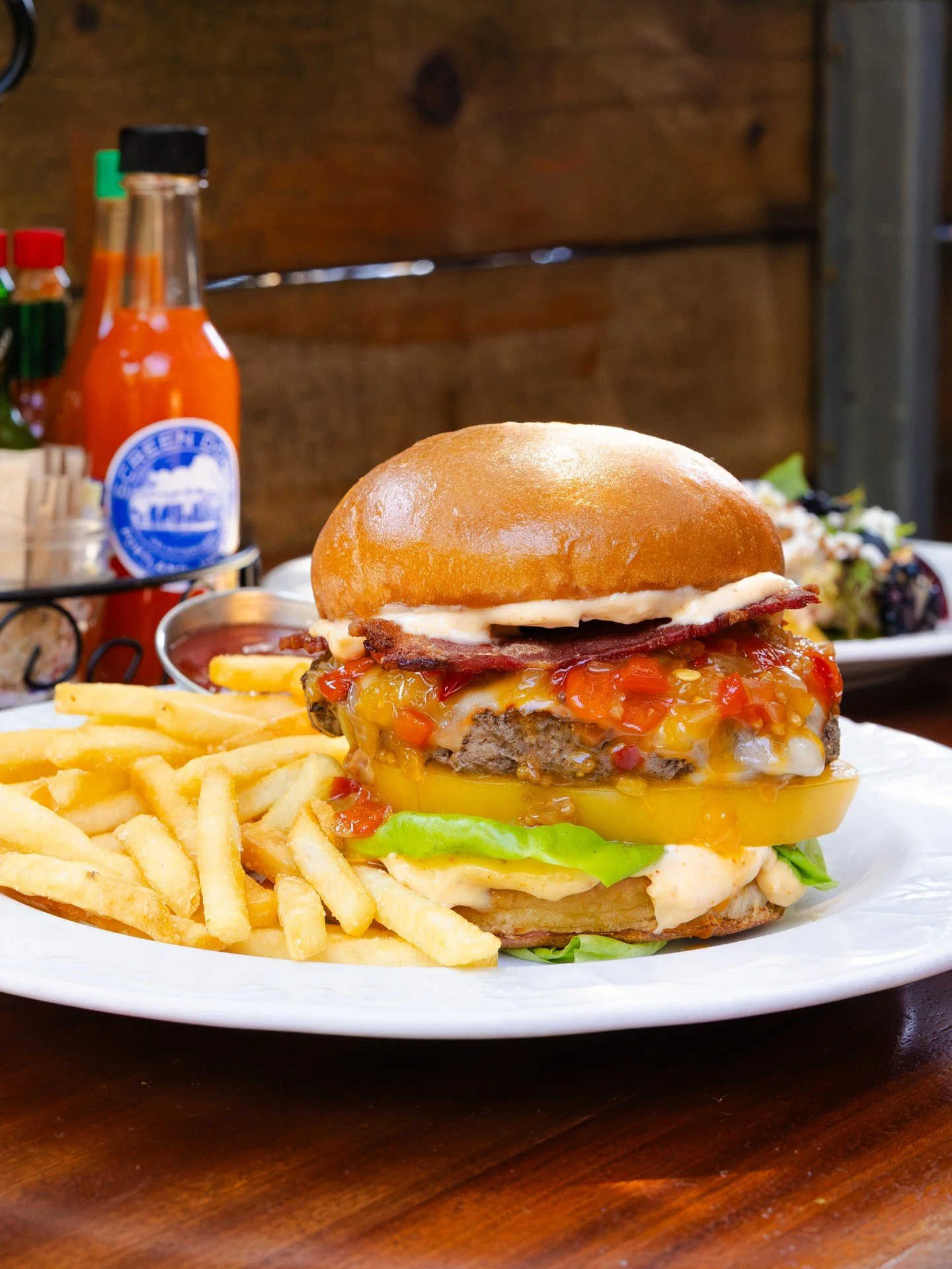 Summer and burgers just go hand in hand. 🍔 Our Bacon &amp; Muenster Burger brings together a 6 oz. griddled beef patty with melted Muenster and applewood-smoked bacon, plus heirloom tomato, summer pepper relish, roasted garlic-Aleppo aioli &amp; but