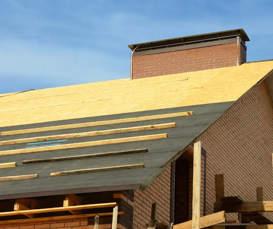 New roof installation showing plywood decking and wooden battens near a brick chimney on a Lacey Township, NJ home