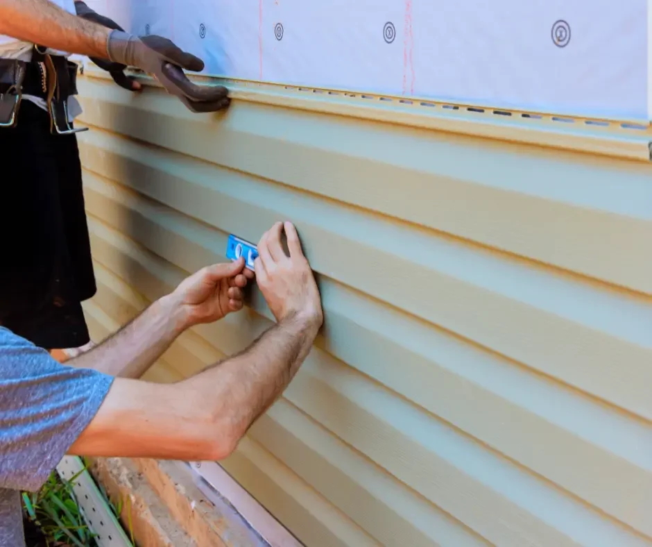 Close-up of GRM Roofing installers locking beige vinyl siding panels into place in Little Egg Harbor, NJ