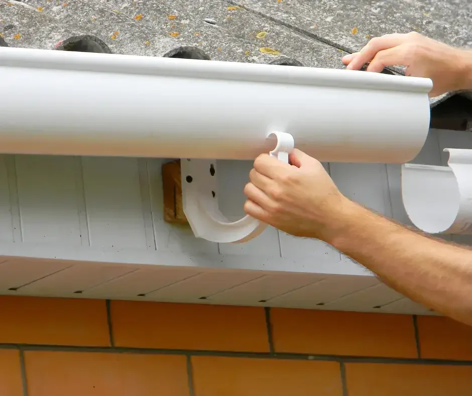 Hands securing a white gutter bracket to a residential roofline for gutter repair in Ocean County NJ