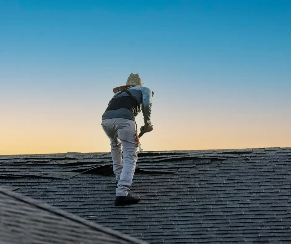 Roofer removing damaged shingles from a rooftop at sunset on a Long Beach Island, NJ home