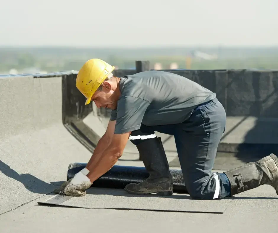 Roofer in yellow hard hat rolling out waterproof membrane material on a commercial flat roof