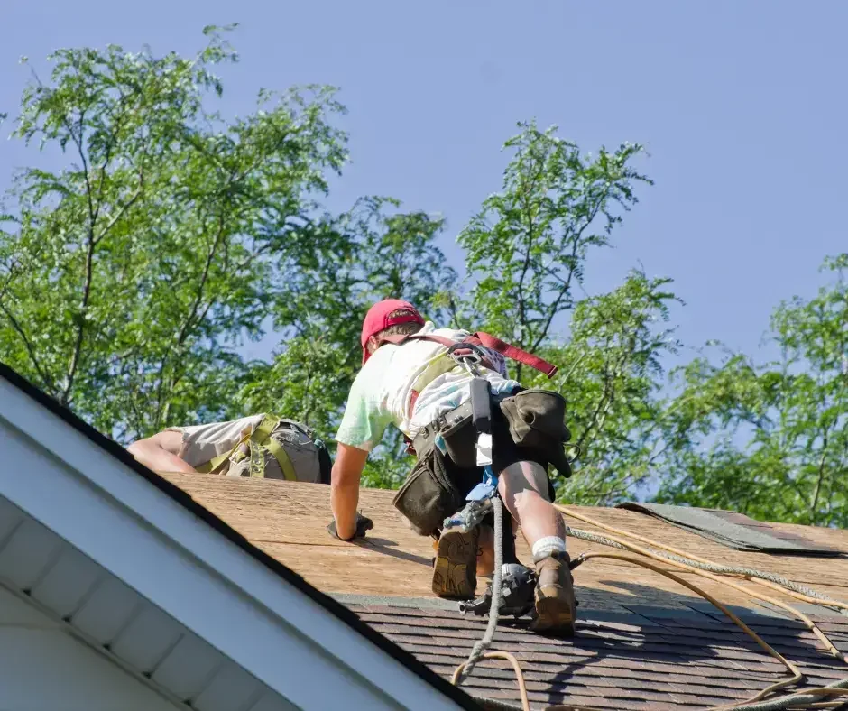 Roofer with tool belt working on a roof repair near the ridge of a Lacey Township, NJ home