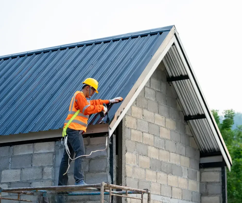 Roofing professional in safety gear checking metal roof flashing and edge trim during a preventive maintenance inspection