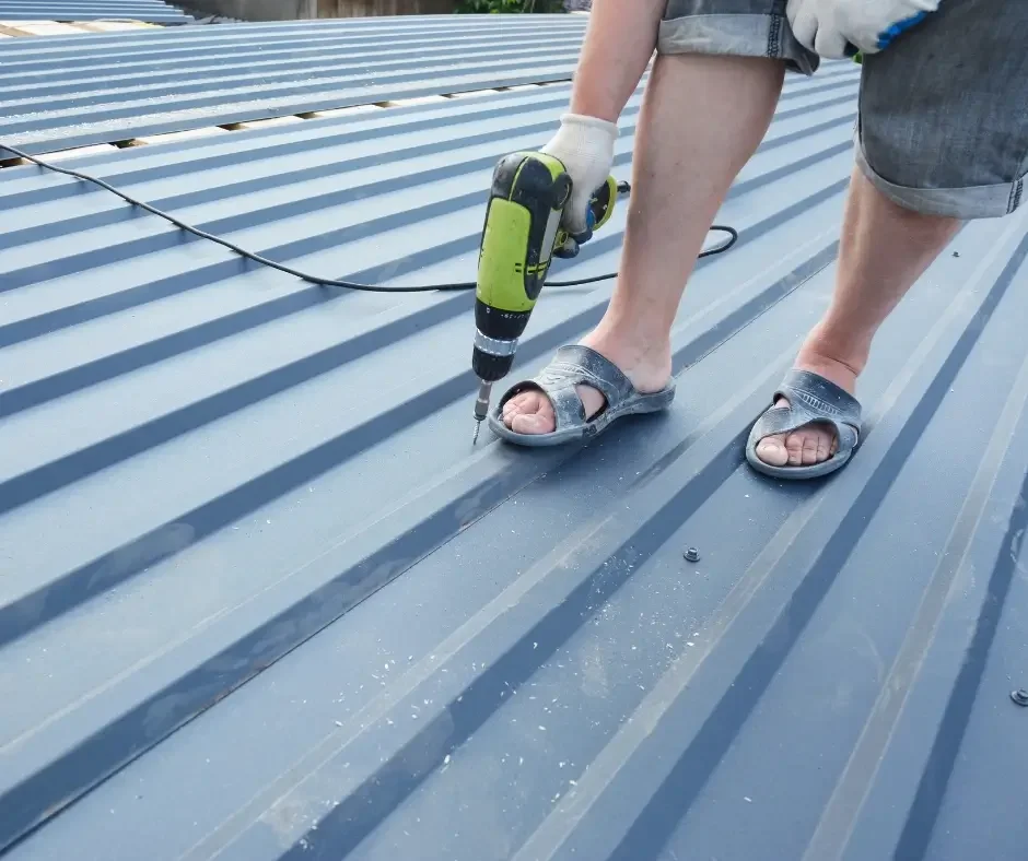 Worker fastening standing seam metal roof panels with a power drill during a roof installation in Toms River NJ