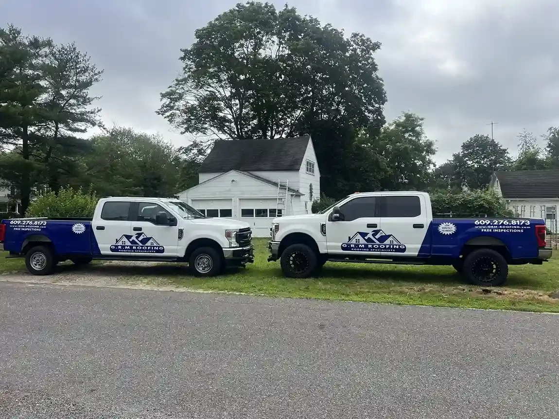 Two GRM Roofing branded work trucks parked in front of a residential home in Ocean County, NJ
