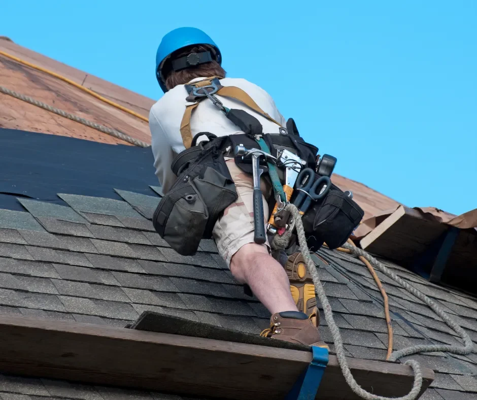 Roofer with a tool belt and safety harness installing asphalt shingles over underlayment in Ocean County NJ