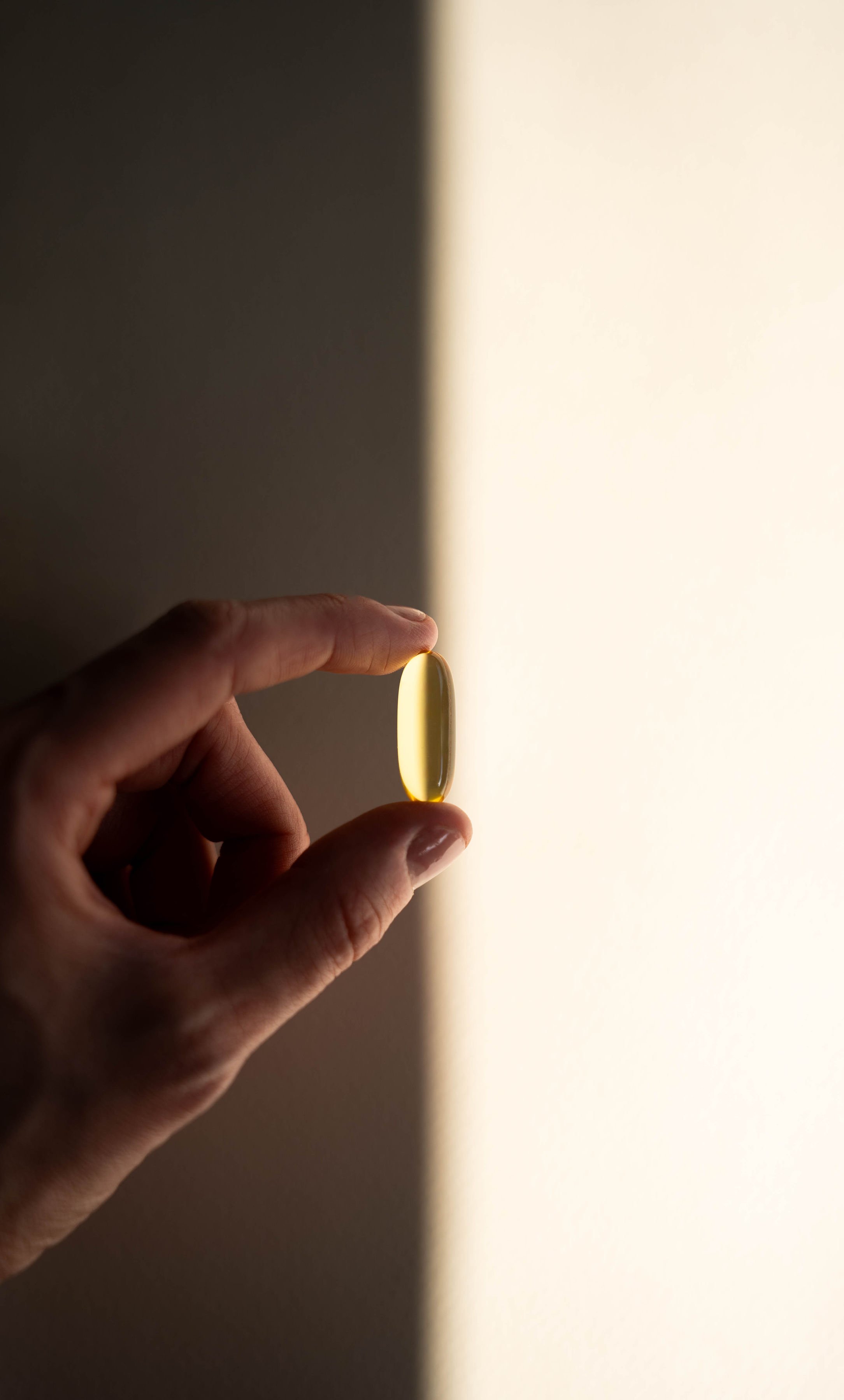 A hand holding a yellow capsule pill against a background divided into light and shadow.