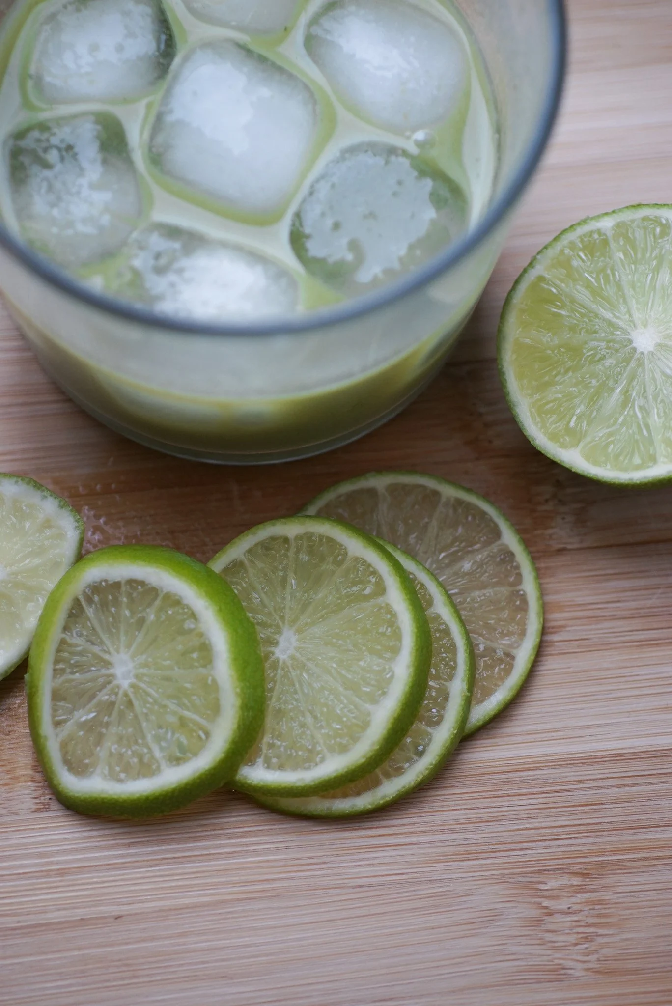 A glass of limeade with ice cubes and a slice of lime on a wooden surface.