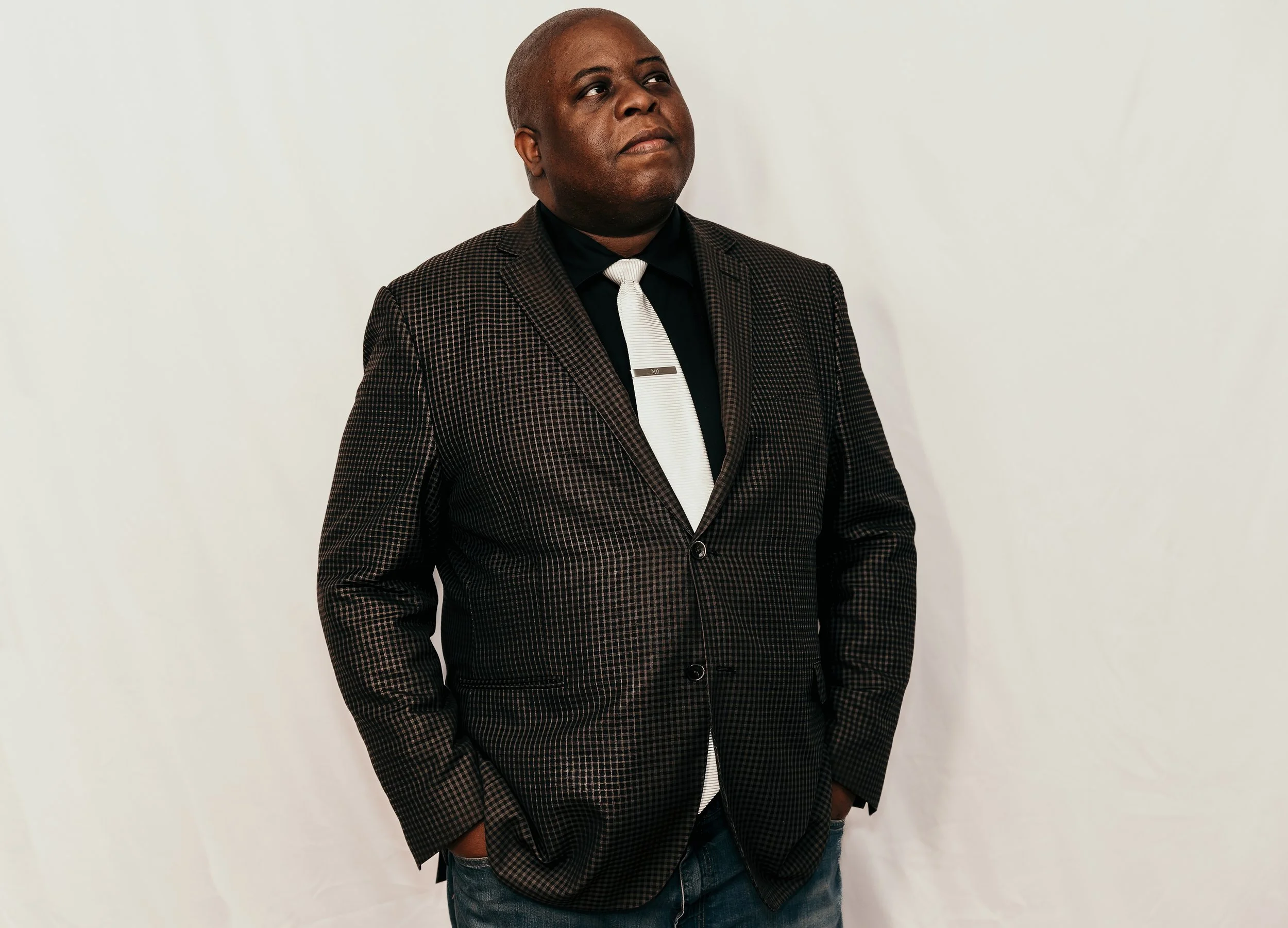 A man with curly dark hair, glasses, and a beard, sitting indoors and smiling slightly.