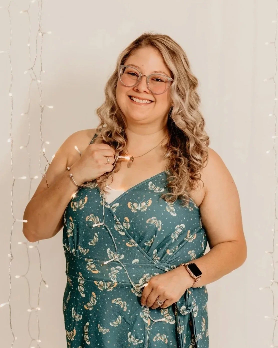 Smiling woman with natural curly hair wearing glasses, hoop earrings, layered necklaces, and a striped blouse.
