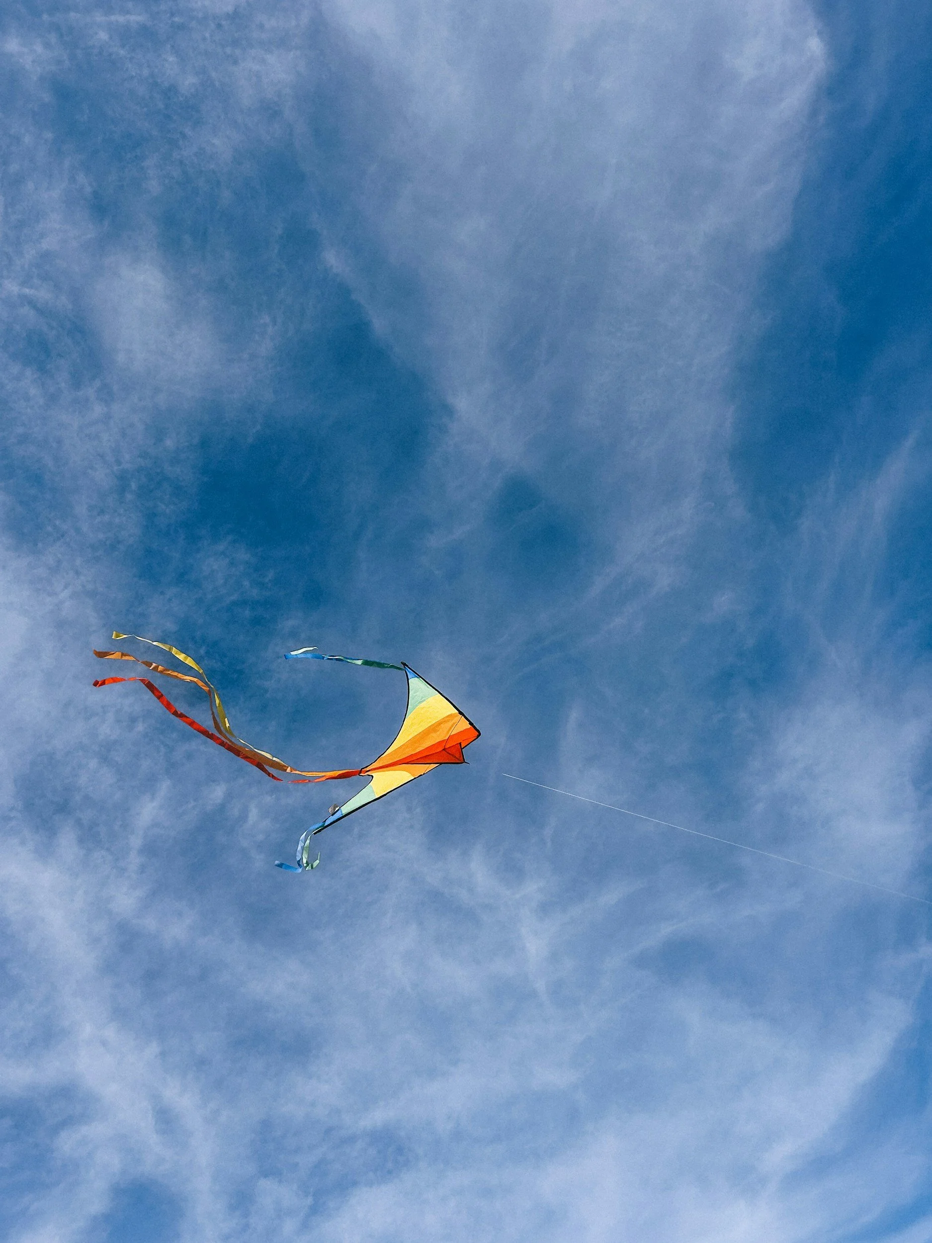 A multi-colored kite flying in the wind in the open sky with a few wispy clouds