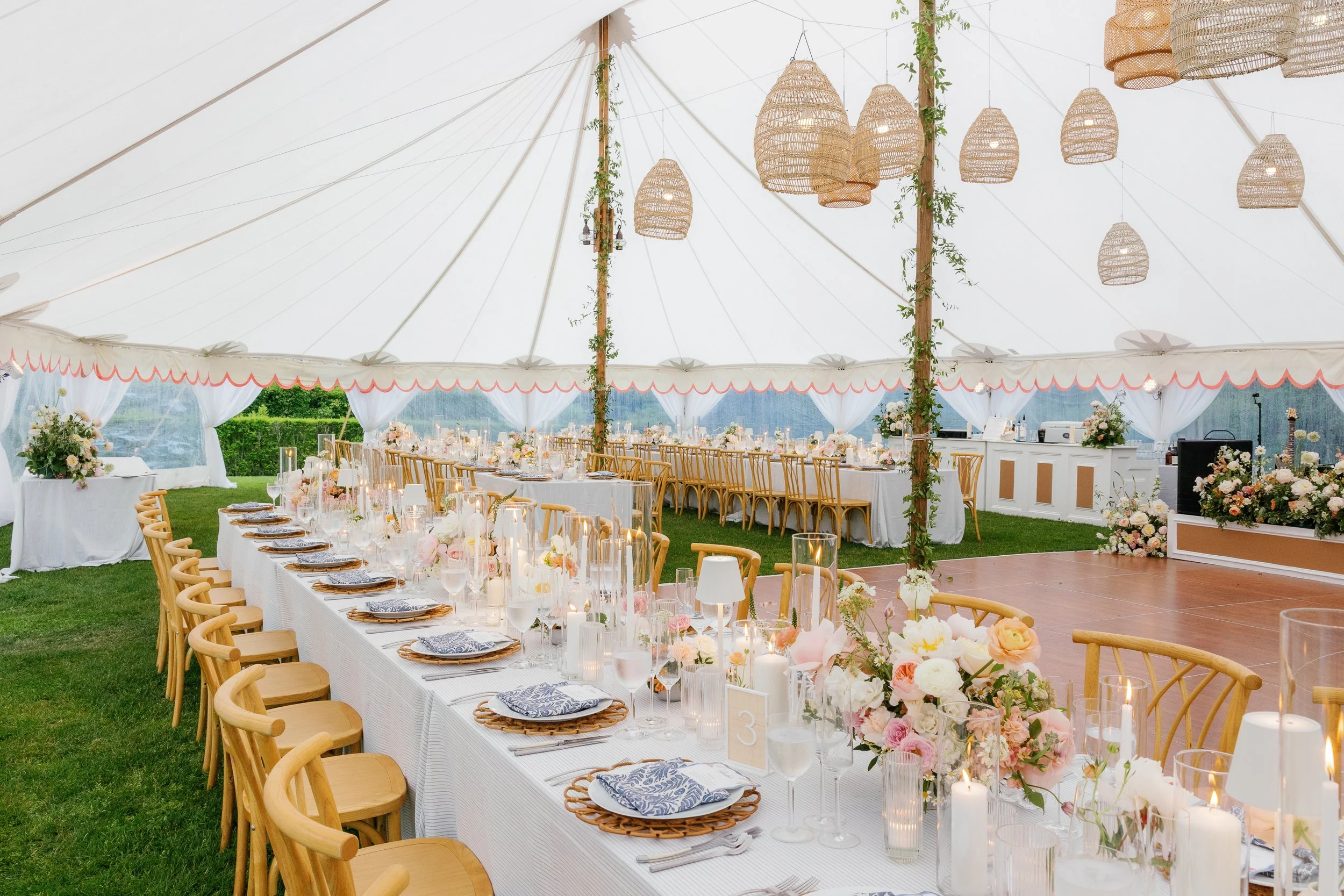 Group of women in colorful dresses enjoying a sunny day outside a gray shore house with white trim, holding white flowers, and smiling at each other.