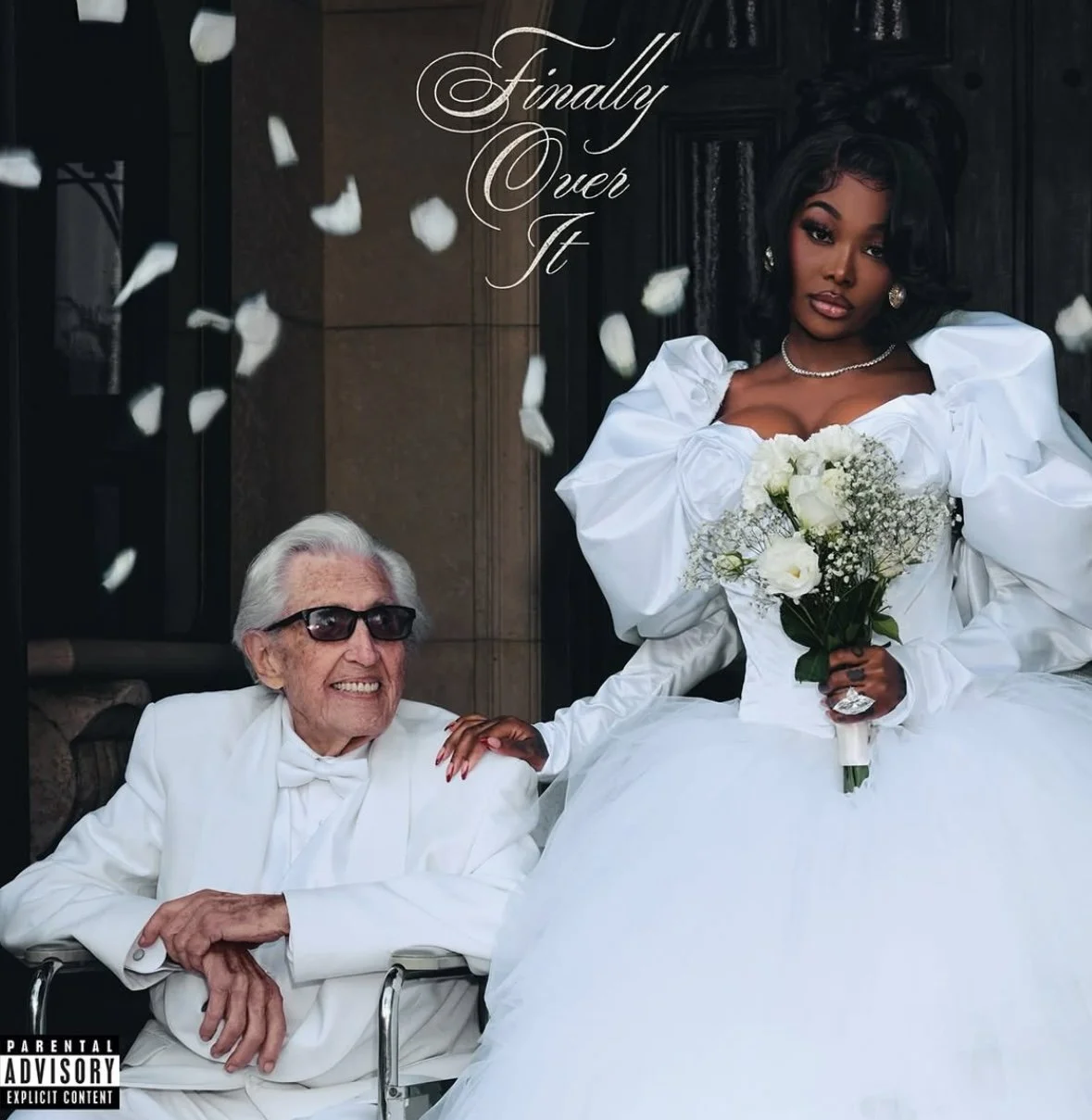 A bride in a white wedding dress holding a bouquet of flowers, sitting with an elderly man in a wheelchair, both smiling. Falling white petals surround them, and the words 'Finally Over It' are written in the top left corner.