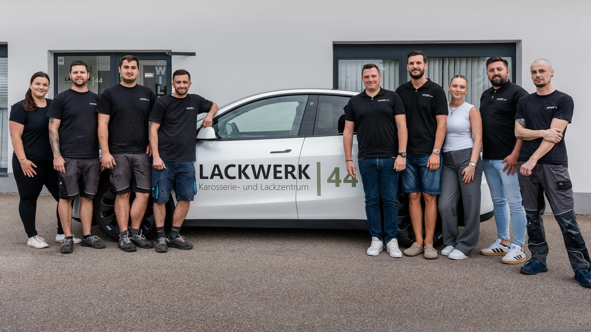 Team von Lackwerk Karosserie- und Lackzentrum steht vor einem weißen Fahrzeug mit Lackwerk-Aufkleber