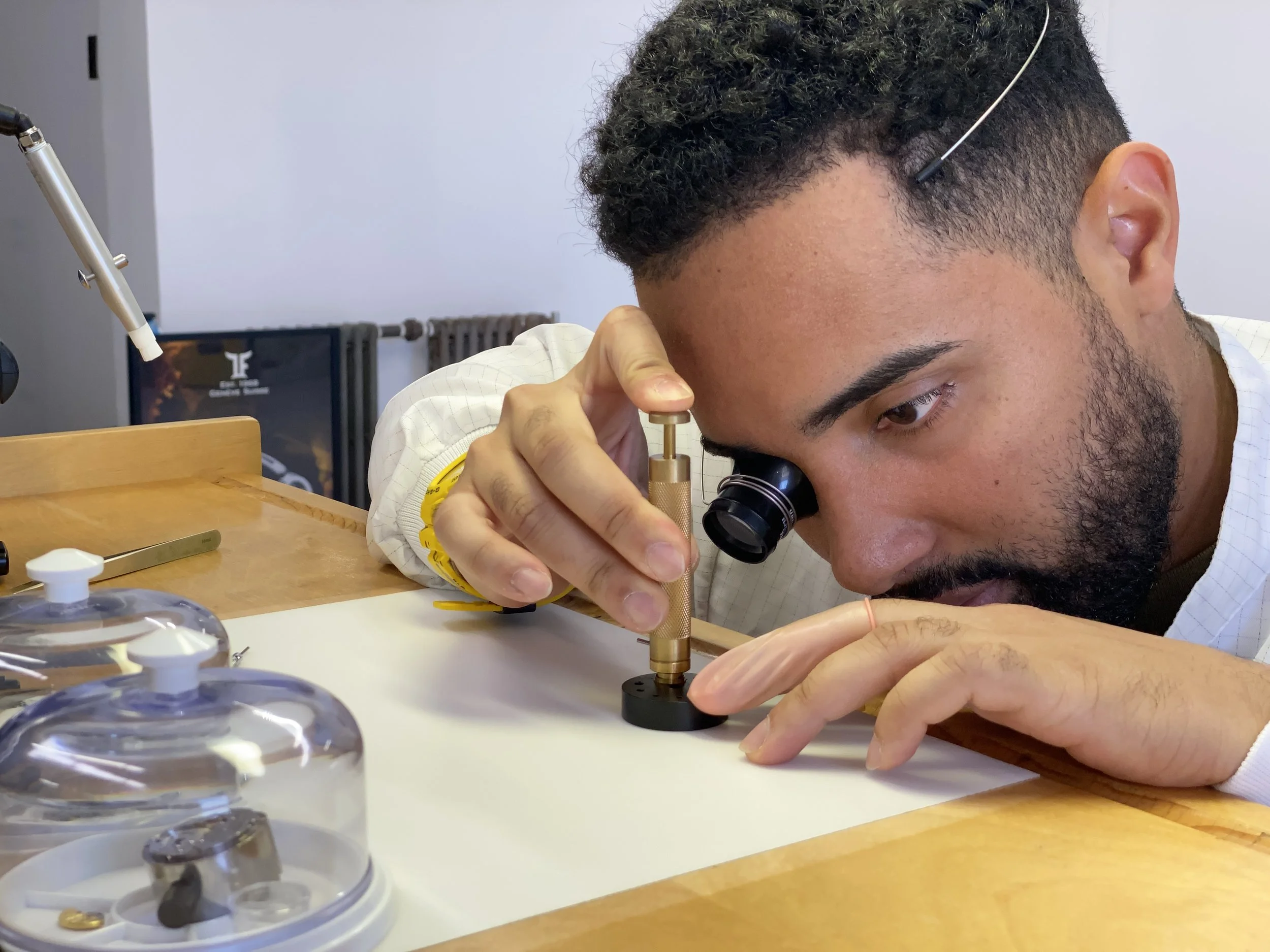 A man wearing a white lab coat using a microscope at a wooden table, with laboratory equipment around him.