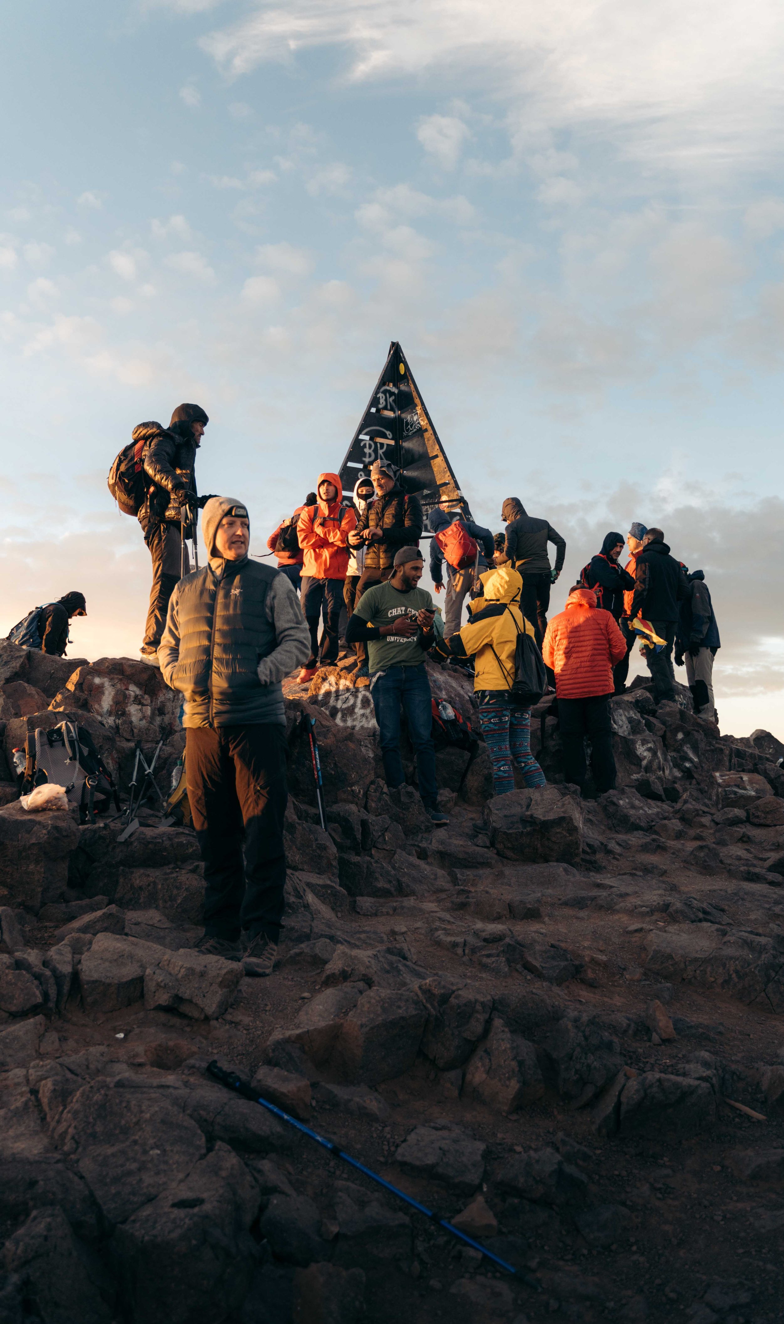 Grupo de personas en la cima de una montaña con una pirámide de metal en el fondo.