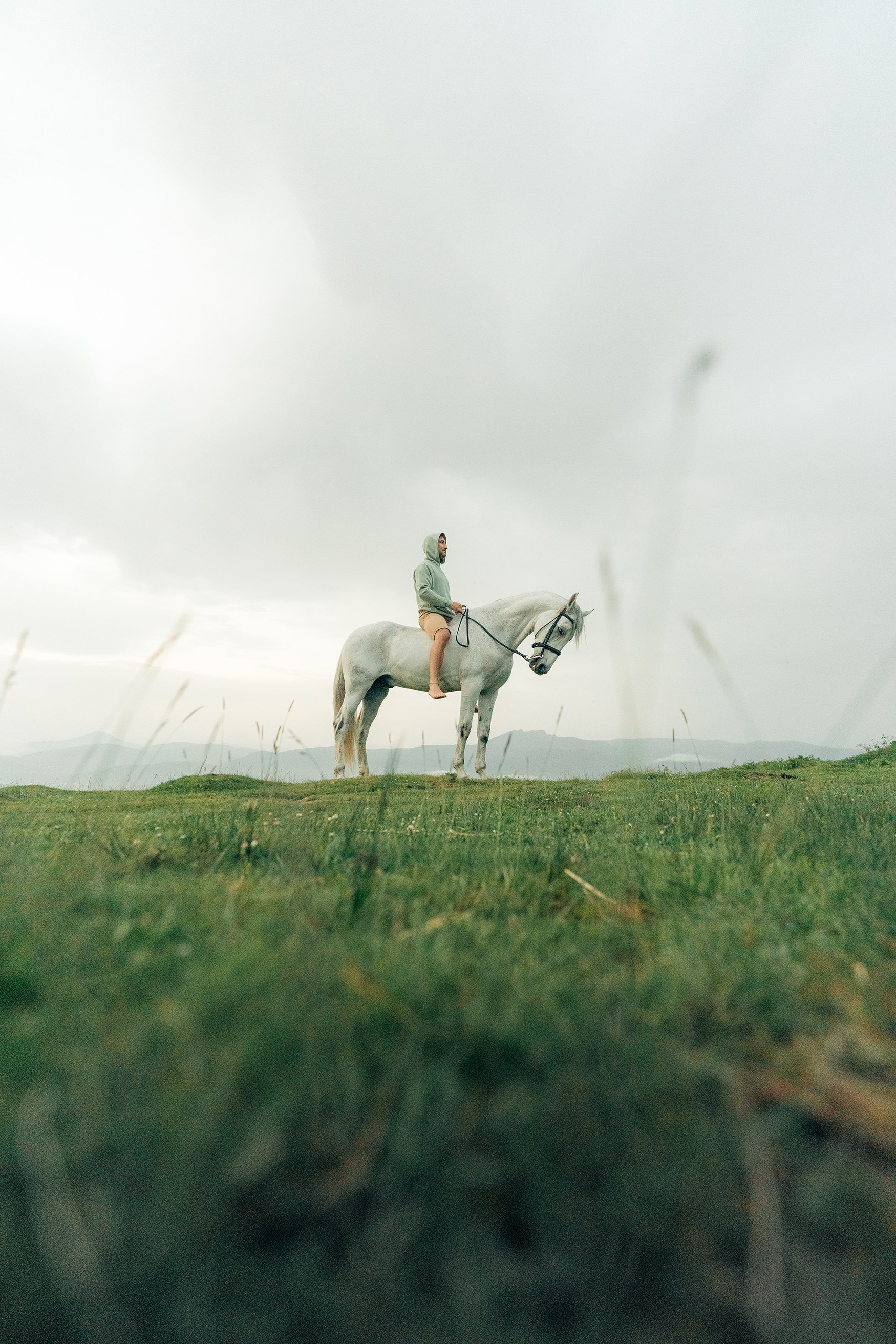 Persona montando un caballo blanco en un campo verde con fondo nublado.