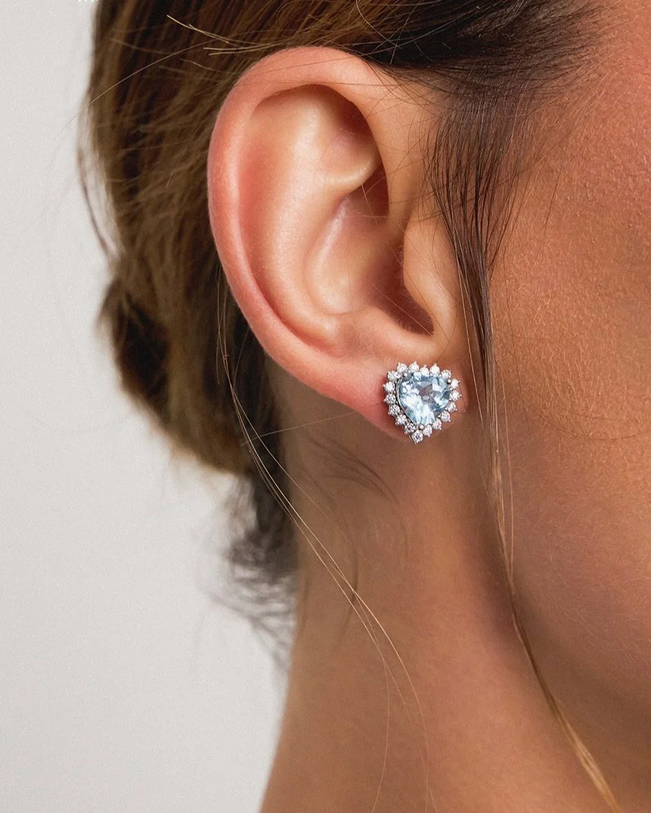 Close-up de uma orelha com brinco de coração com pedras brilhantes.
