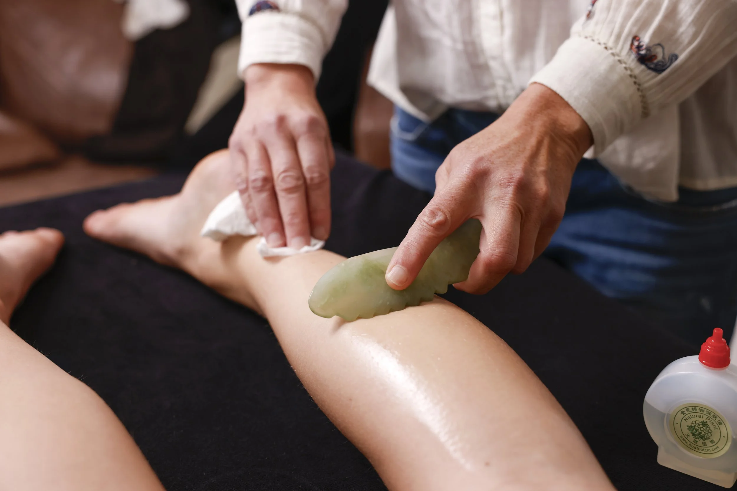 A person receiving a volcanic hot stone massage, with a massage therapist using a heated stone on their leg.