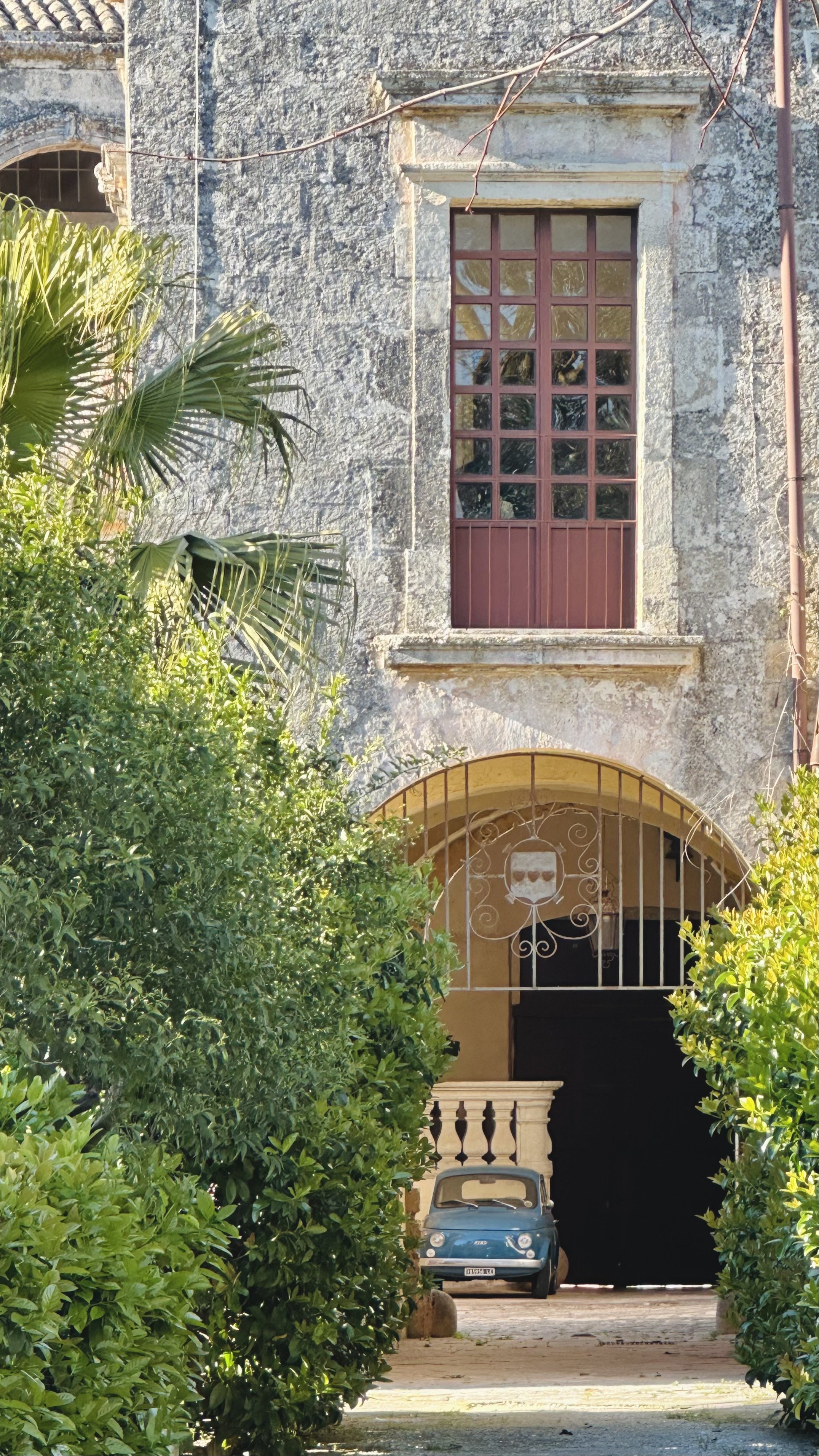 Vintage Fiat 500 parked under a stone archway at Palazzo Bacile in Spongano, Puglia, surrounded by lush greenery and historic southern Italian architecture