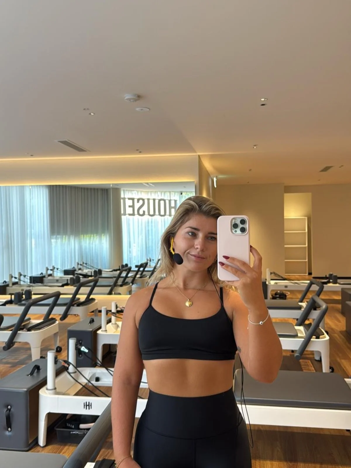 A woman taking a selfie in a fitness studio, with mirrors and exercise equipment visible in the background.
