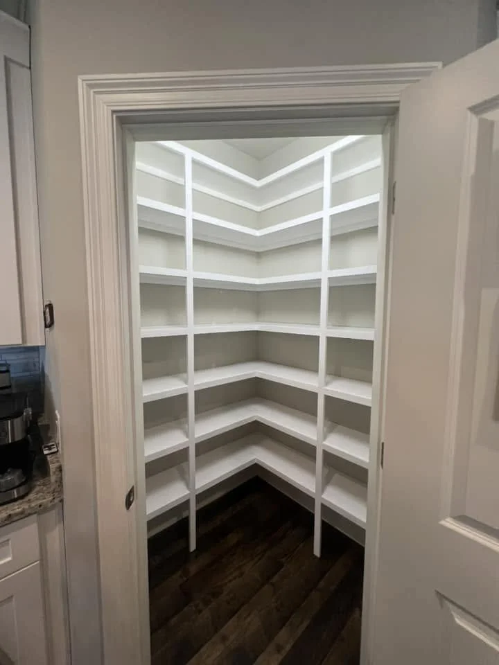 Empty white corner pantry with multiple shelves and dark wood floor.