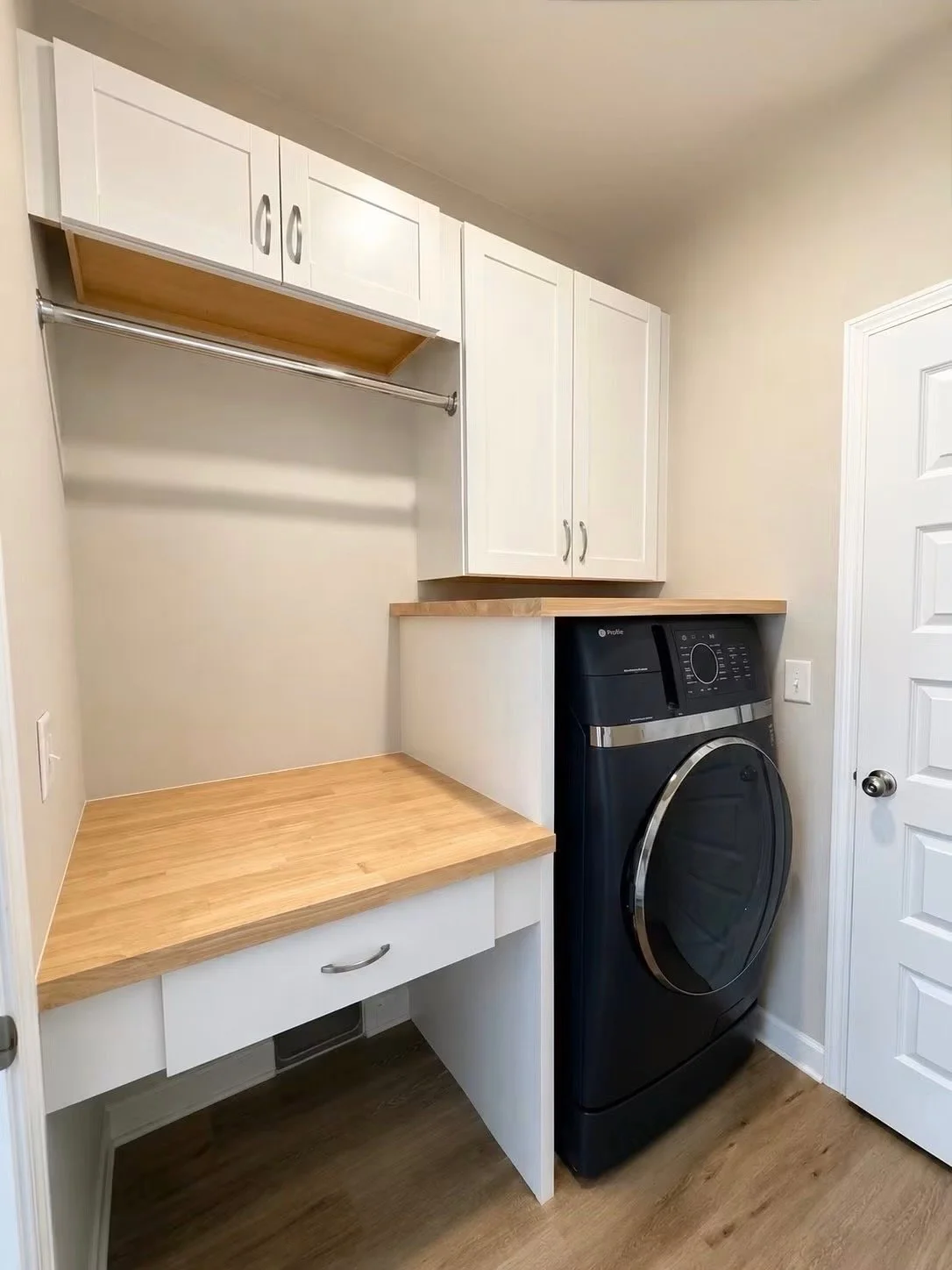 Laundry room with white cabinets, wooden countertop, and a black front-loading washing machine.