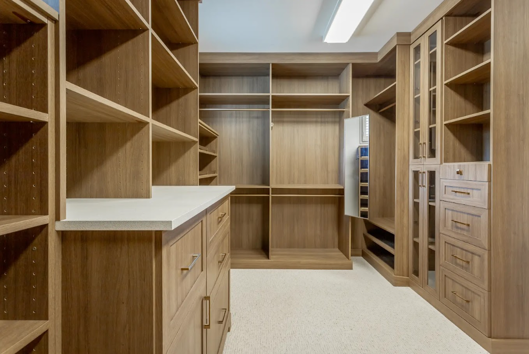 A spacious walk-in closet with wood shelves, drawers, and cabinets for storage.