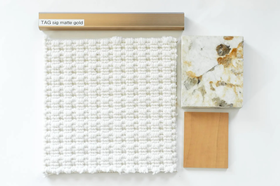 Sample board including a beige tag with a label, a white textured fabric, a marble sample, and a small wooden tile.