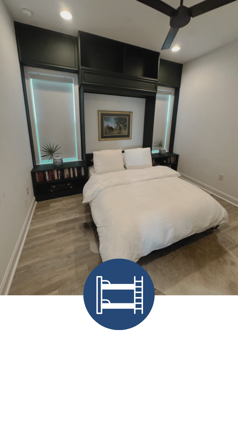 A bedroom with a white bed, black built-in shelves and headboard, a framed painting on the wall, two nightstands with books and potted plants, and ceiling fans with lights.