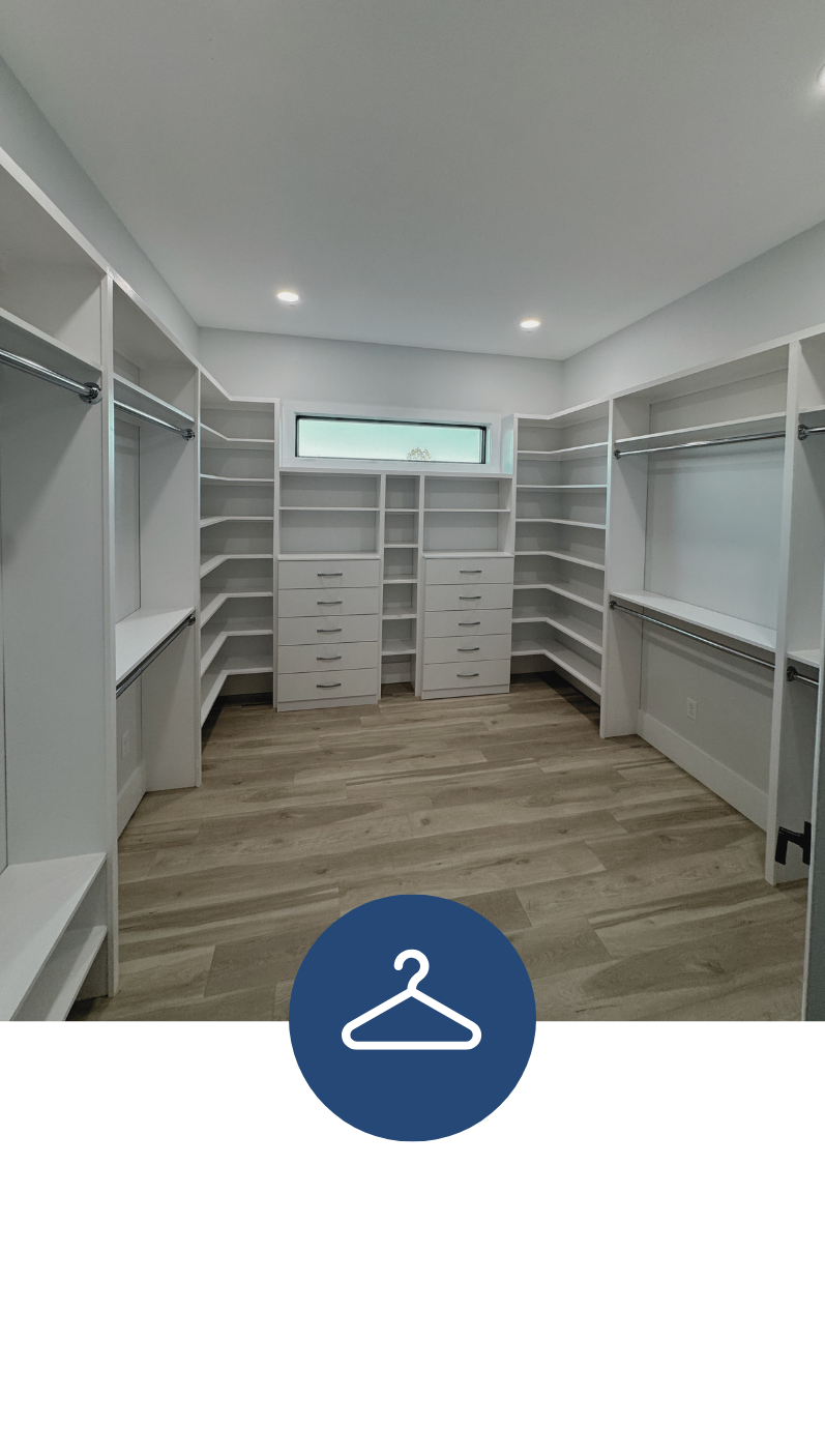 Empty walk-in closet with white built-in shelves and drawers, metal hanging rods, a small horizontal window, and hardwood floors.
