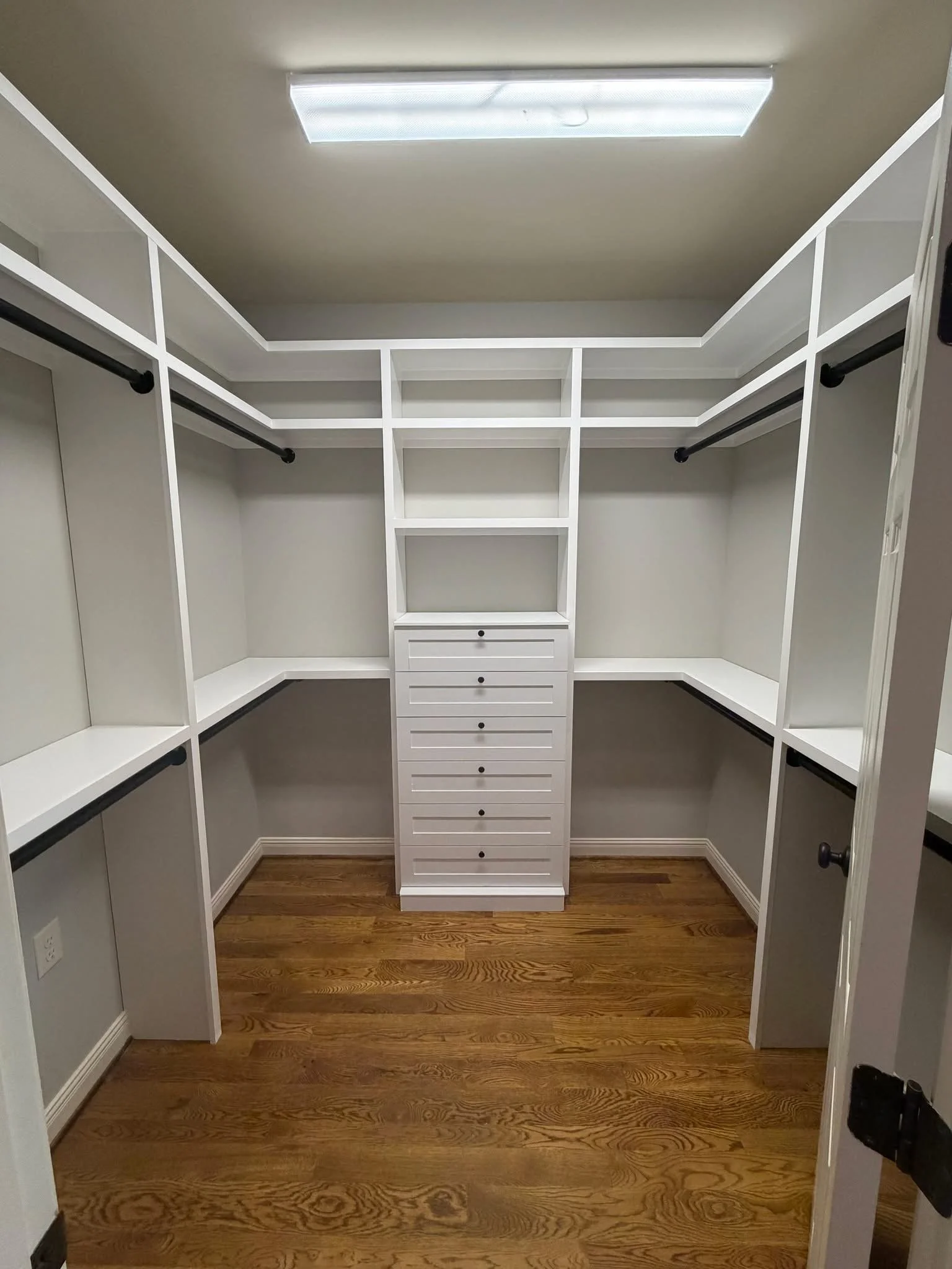 Empty walk-in closet with white shelves and drawers, black hanging rods, and hardwood flooring.