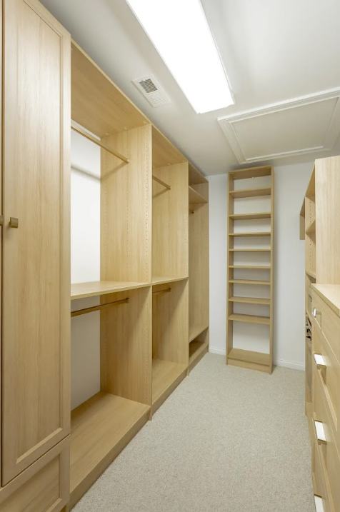 Empty wooden closet and shelving units in a walk-in closet with beige carpet and white walls.