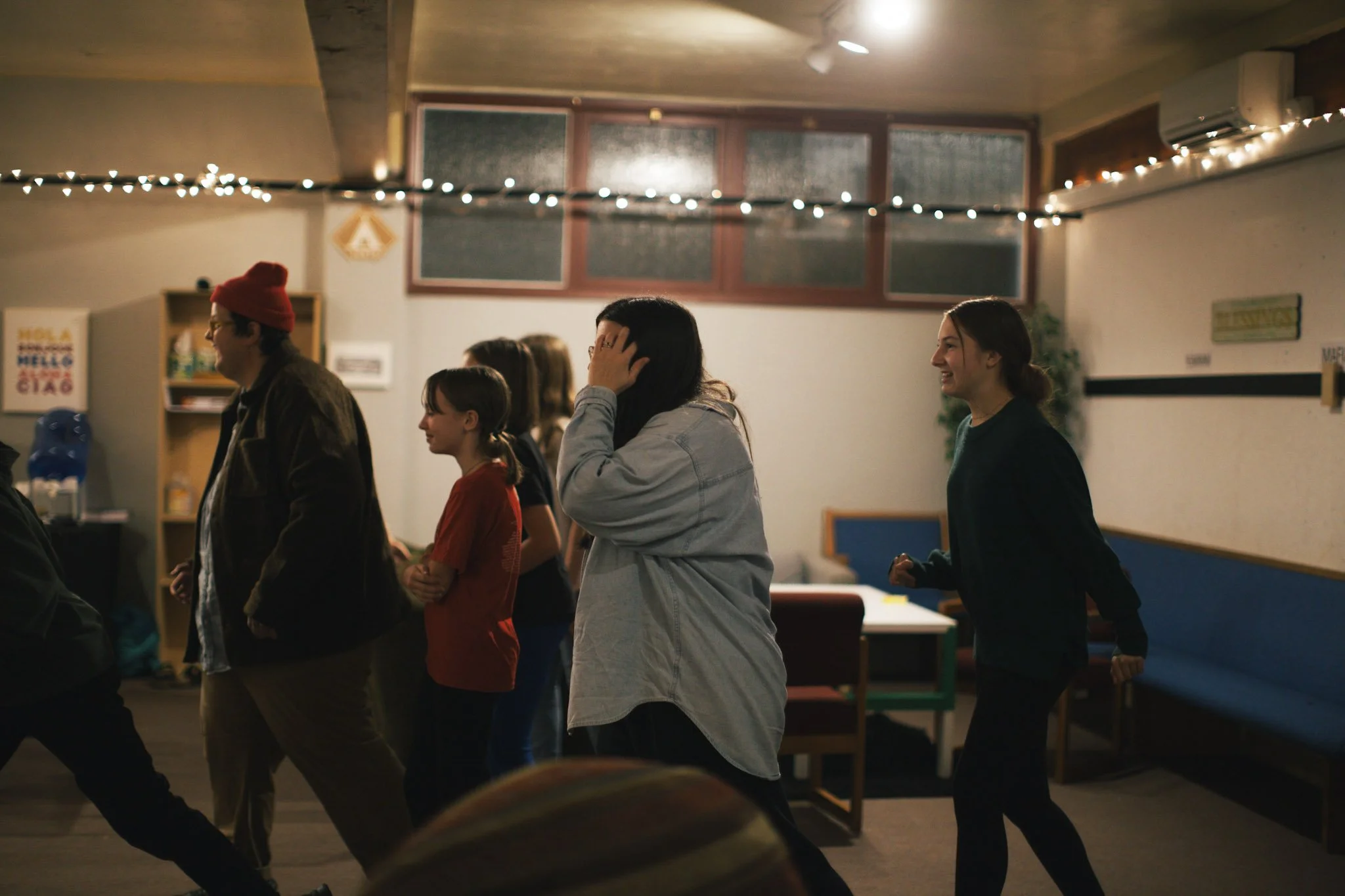 Children and adults playing baseball on a grassy field with trees in the background.