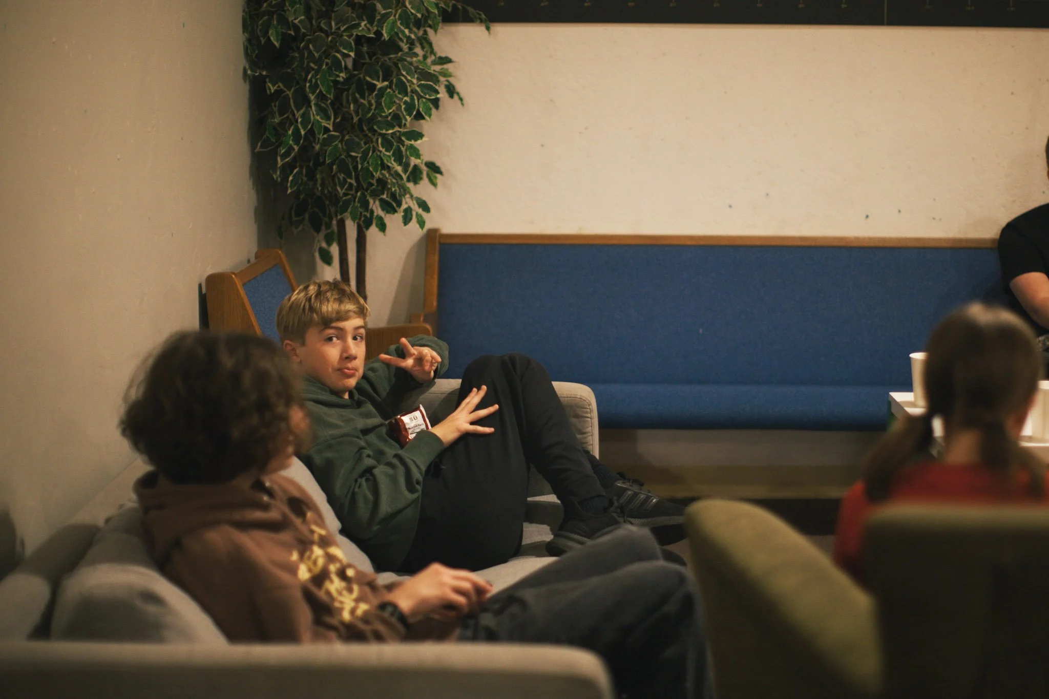 Four people walking on the beach near driftwood and rocks, with houses and a hill in the background.