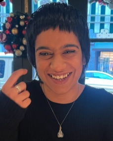 A picture of Pri with short black hair, a black top, smiling at the camera