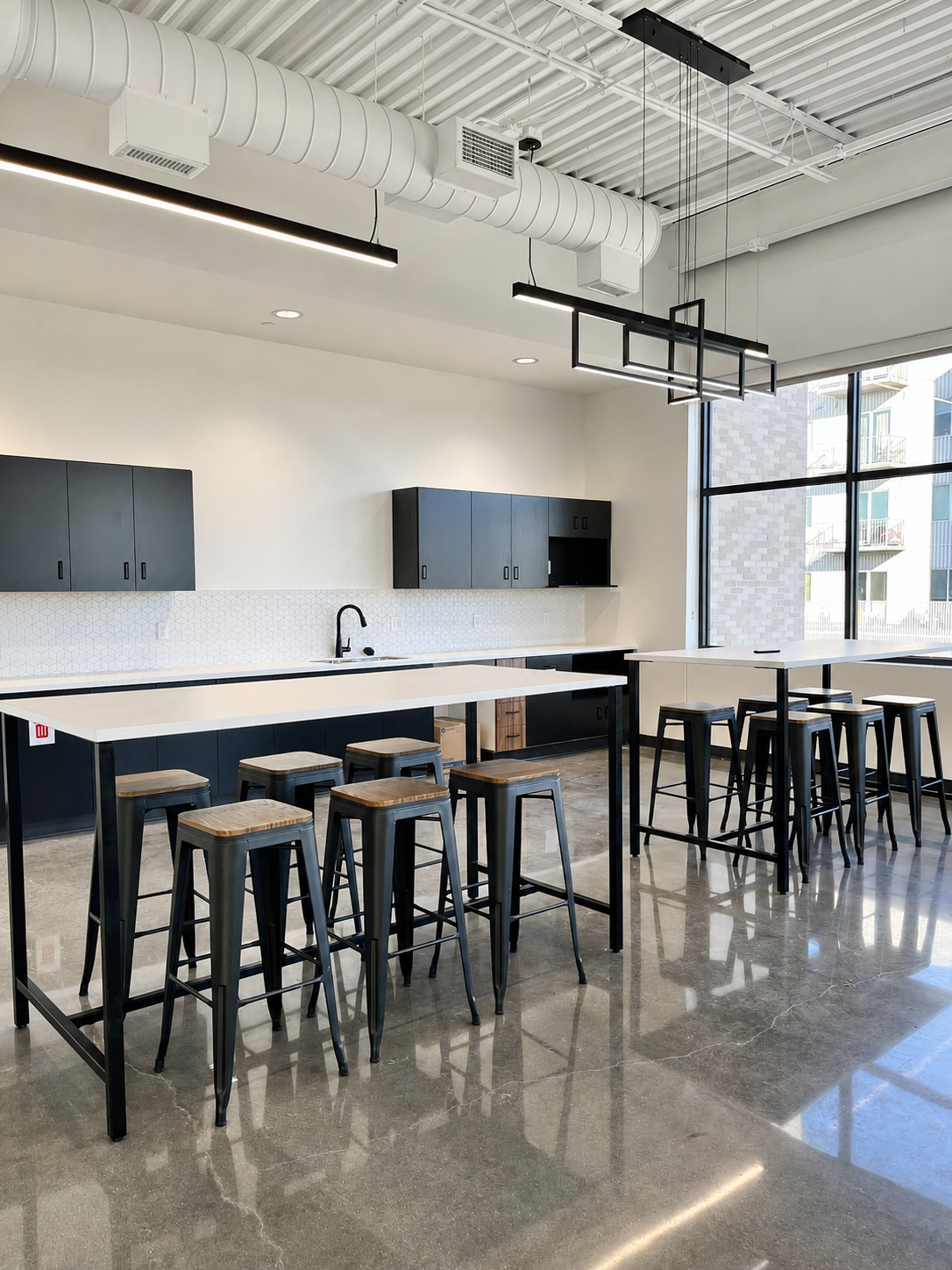Modern kitchen with high tables and stools, black cabinets, and large windows in a bright space