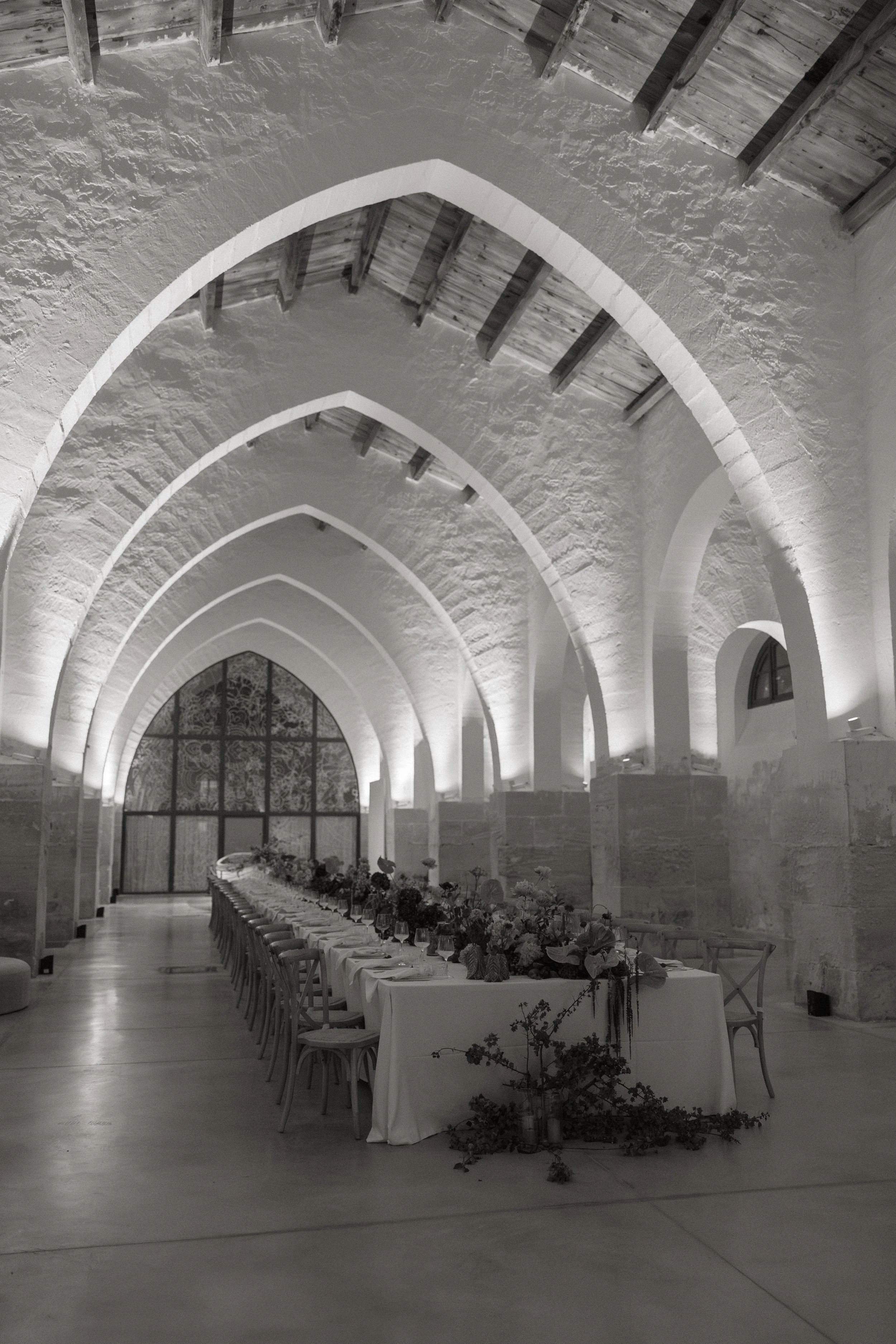 Black-and-white editorial photograph of Camparia Favignana's vaulted wedding reception hall and long floral dining table.